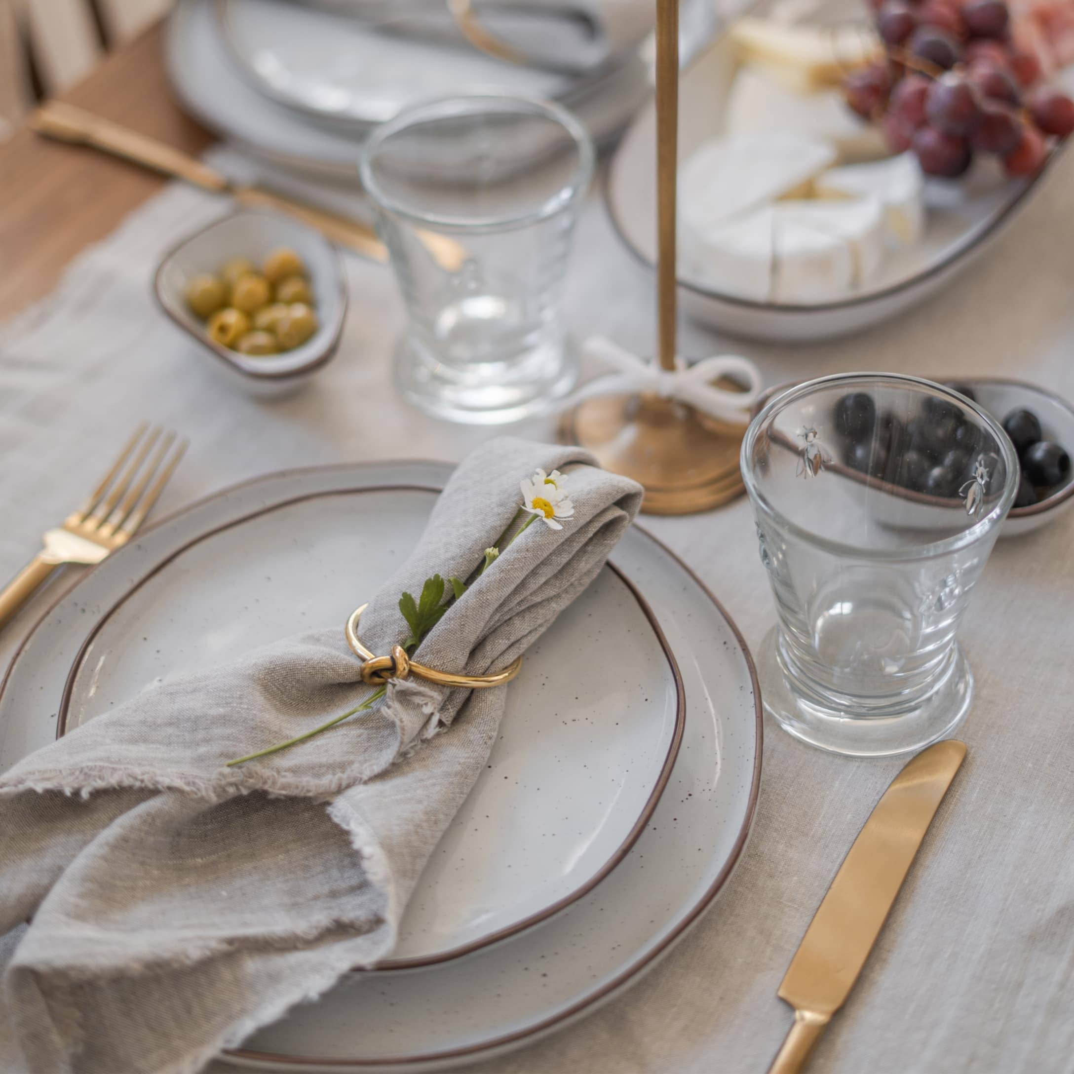 Elegantes Tischgedeck mit grauen Tellern, goldenem Besteck und Leinenserviette mit Blume