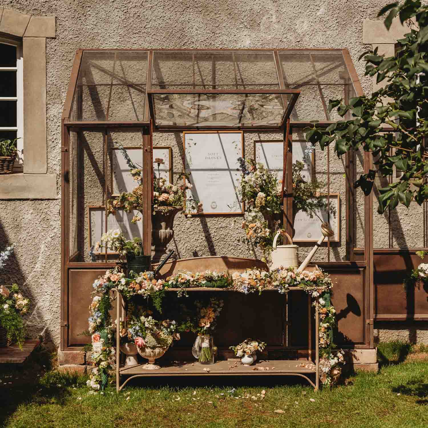 Rustikale Metall-Gartenbank mit Blumenarrangements und Gießkanne vor strukturierter Wand mit Fenster