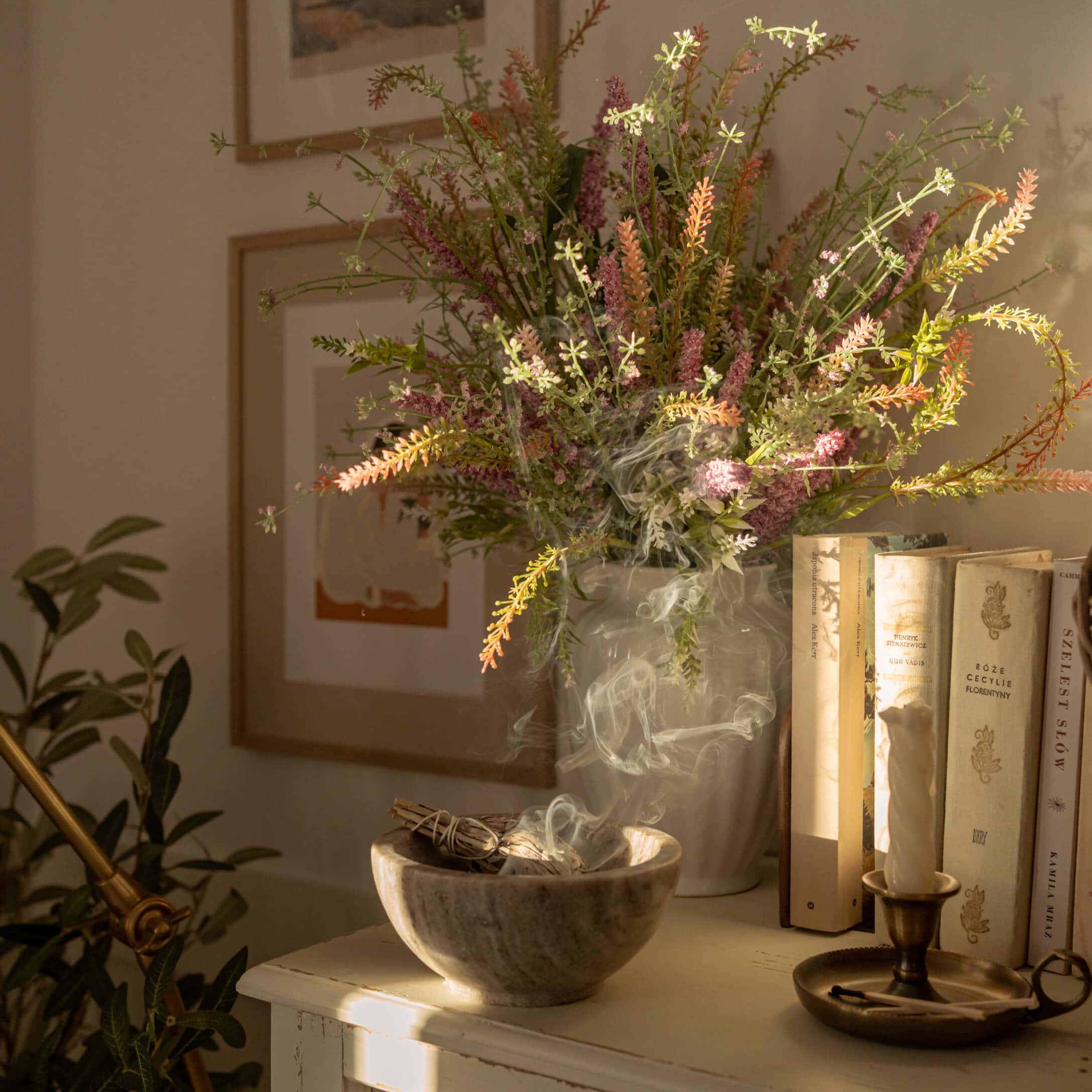 Alabaster-Schale mit rauchendem Salbei neben Vase mit bunten Blumen und Büchern auf Tisch