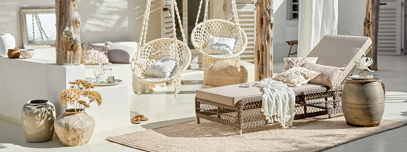 Gemütliche Lounge mit Rattan-Liegestuhl und hängenden Baumwollsesseln in Naturtönen
