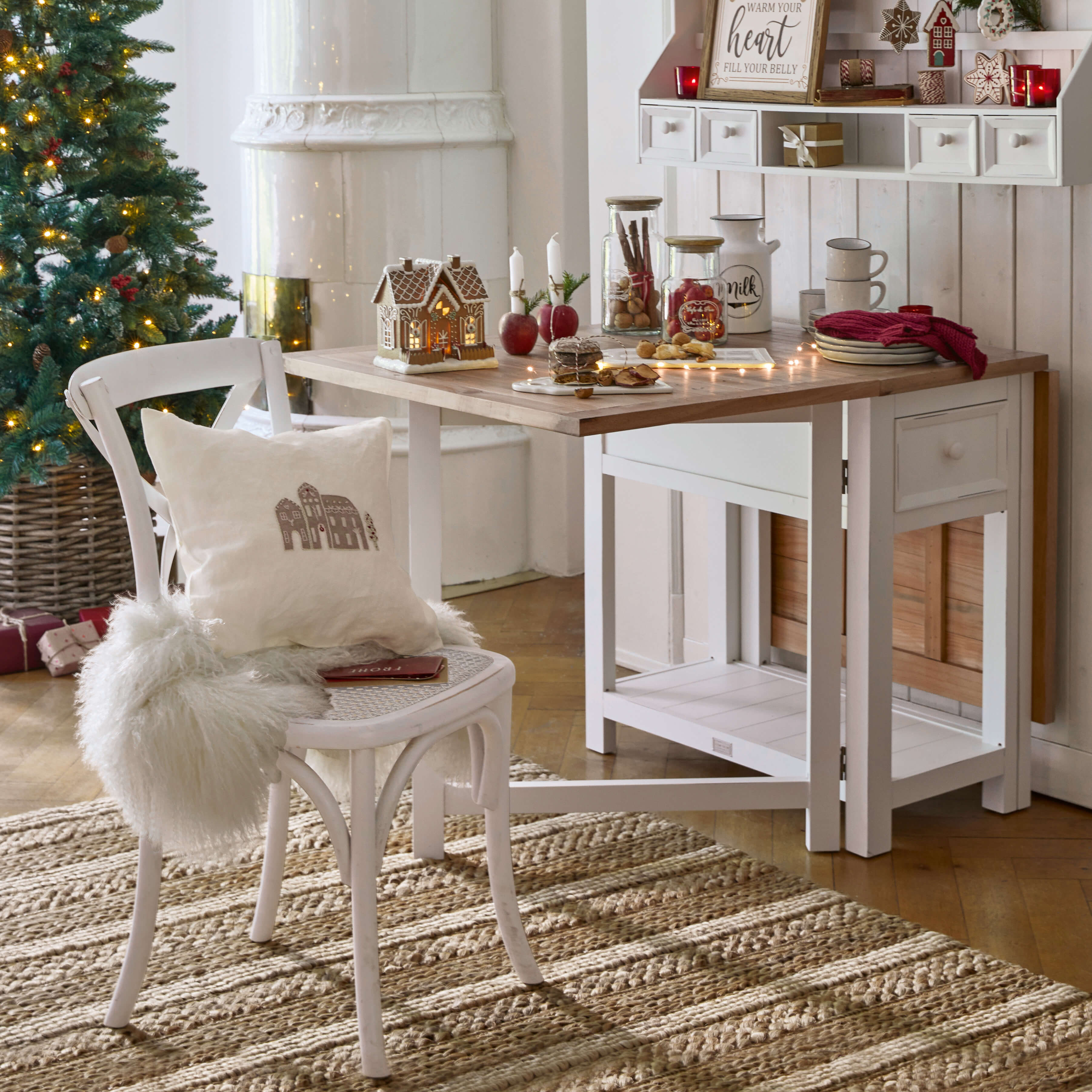 Gemütlicher weisser Holztisch und Stuhl mit Weihnachtsdekoration und beleuchtetem Tannenbaum im Hintergrund