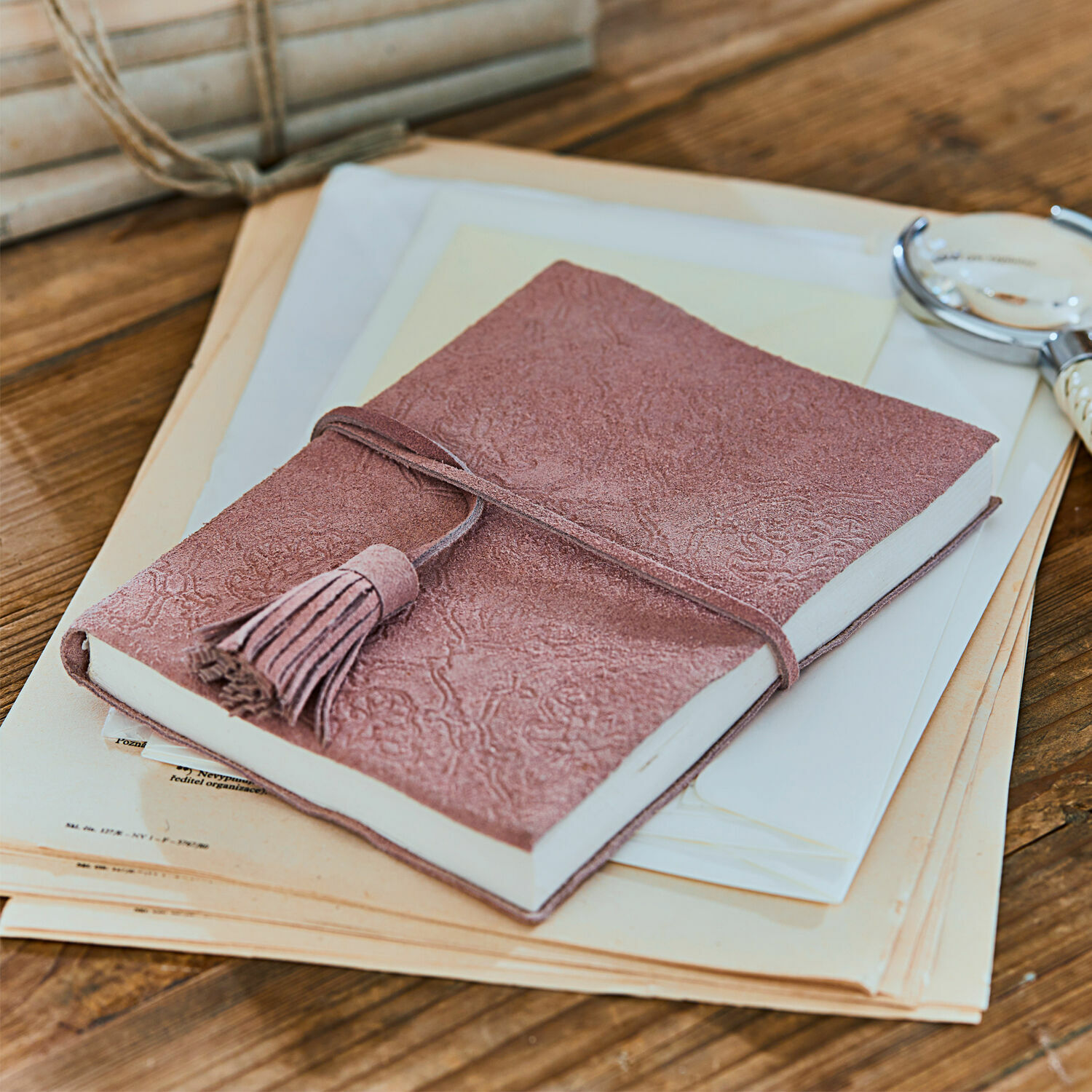Notizbuch Orcival Rosa Notizbuch aus Wildleder mit Quaste auf Holztisch mit Dokumenten und Schreibutensilien