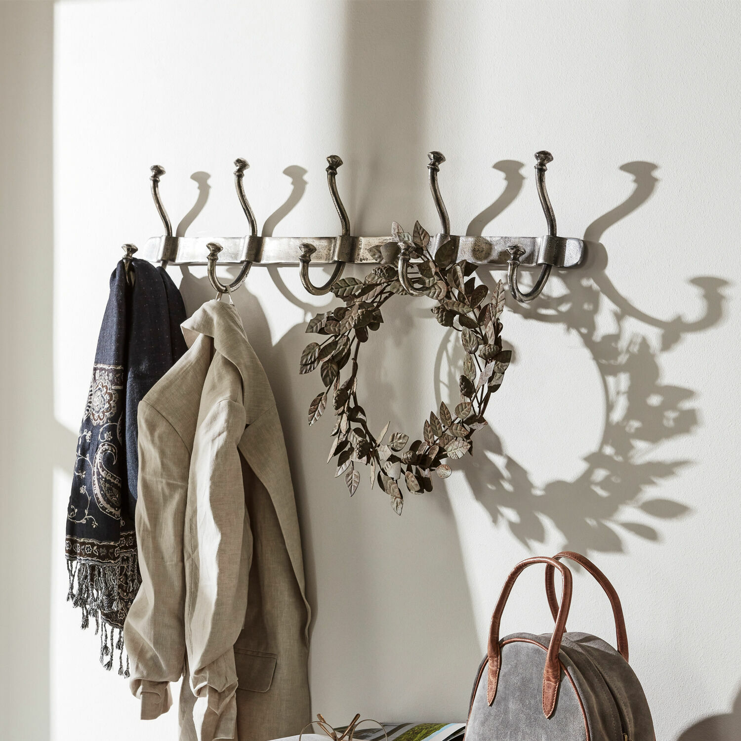 Hakenleiste Pincé Wandgarderobe aus Metall mit acht silbernen Haken, an denen Jacke und Schal hängen.