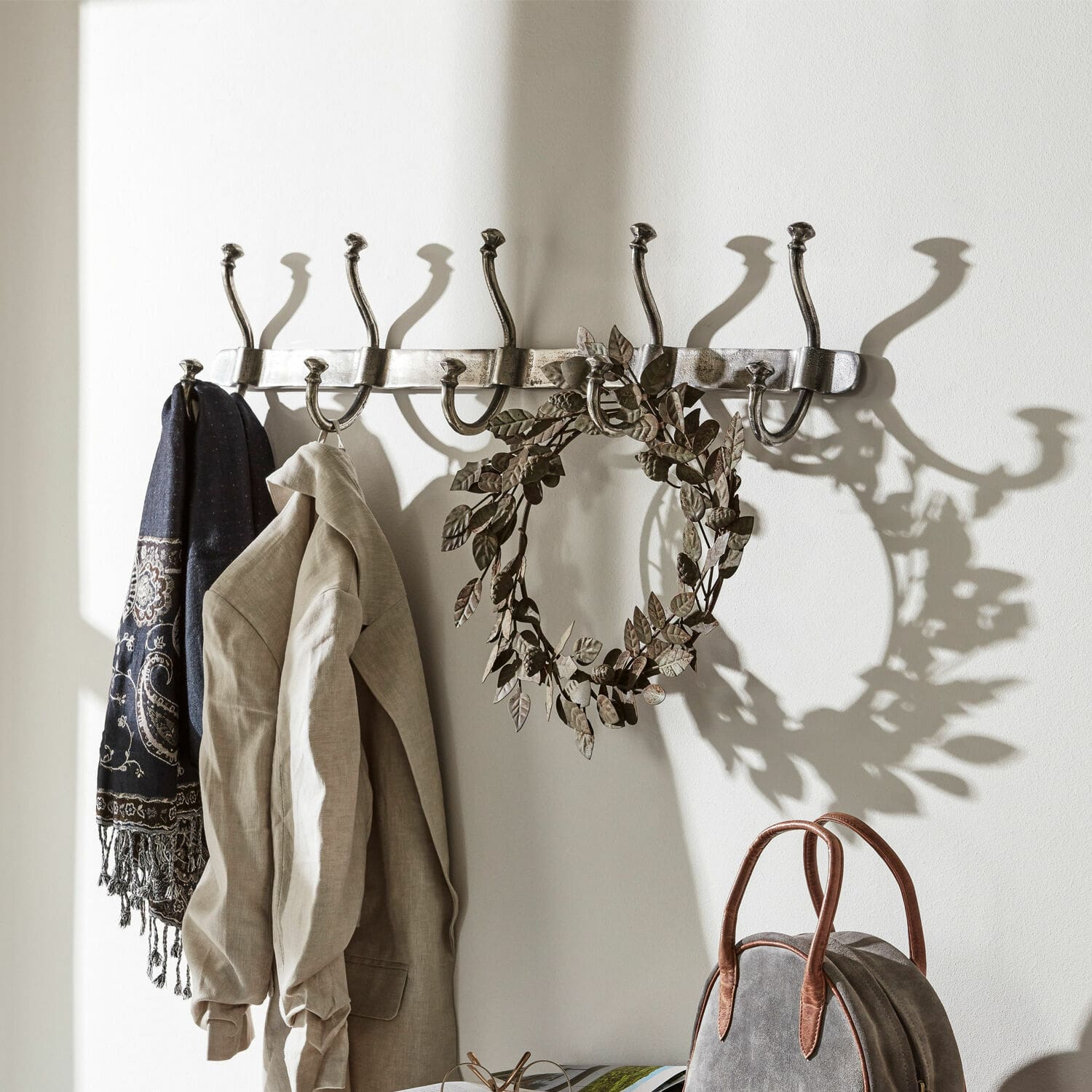 Hakenleiste Pincé Wandgarderobe aus Metall mit acht silbernen Haken, an denen Jacke und Schal hängen.