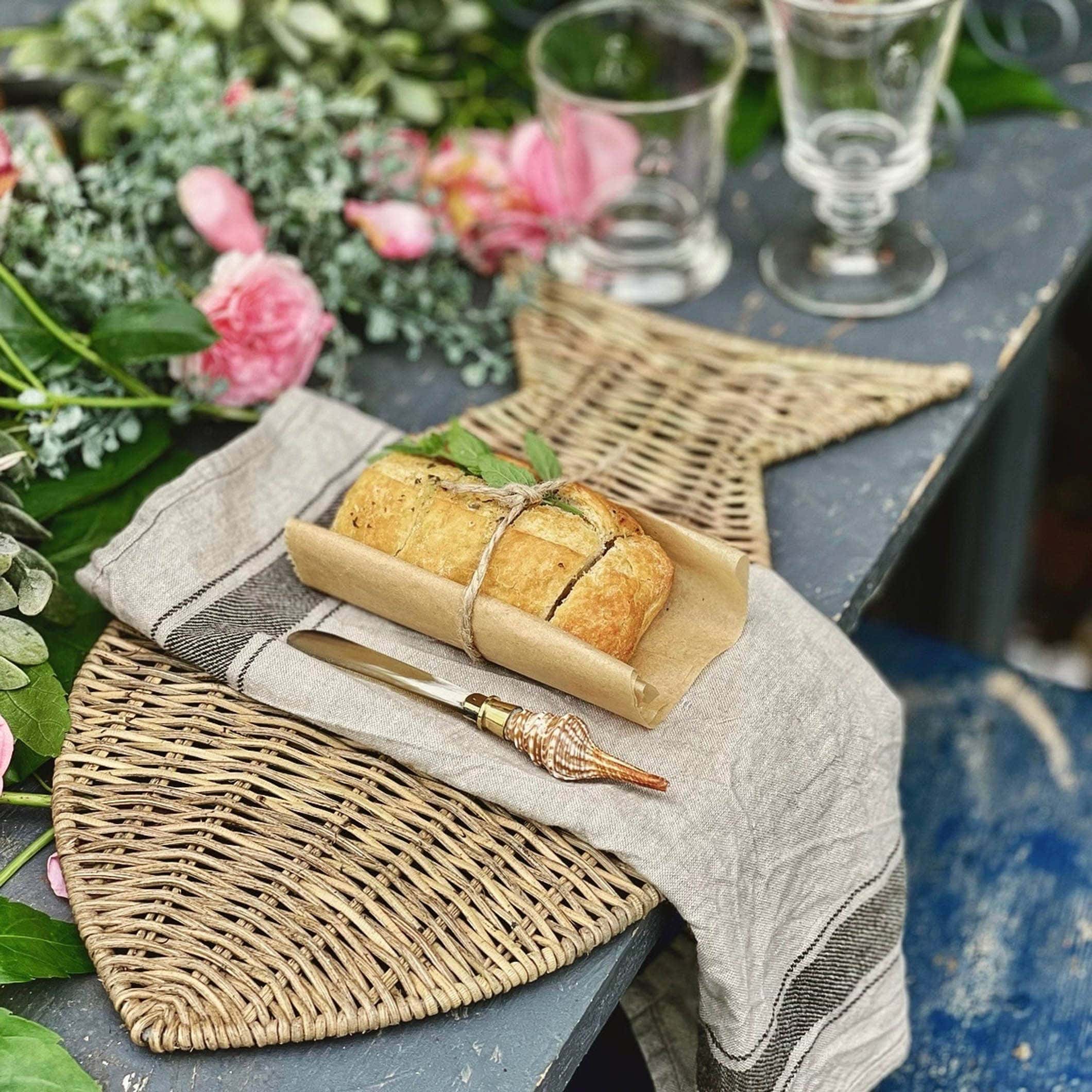 Rustikale Tischunterlage aus Seegras mit Brot und einem Muschelgriffmesser auf einem alten Tisch