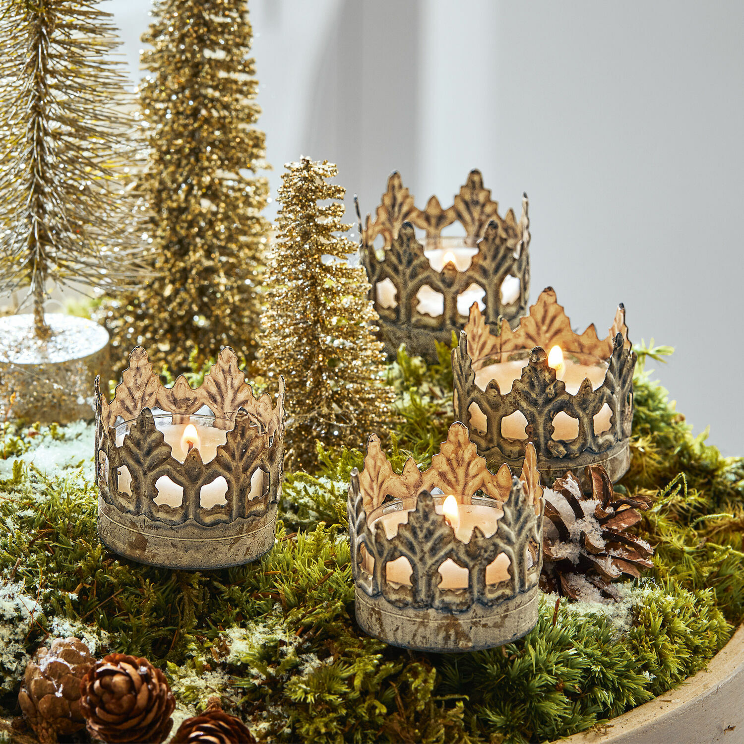 Steckwindlicht 4er Set Groisy Metall-Kerzenhalter in Kronenform auf grünem Moos mit Weihnachtsdekoration und brennenden Kerzen