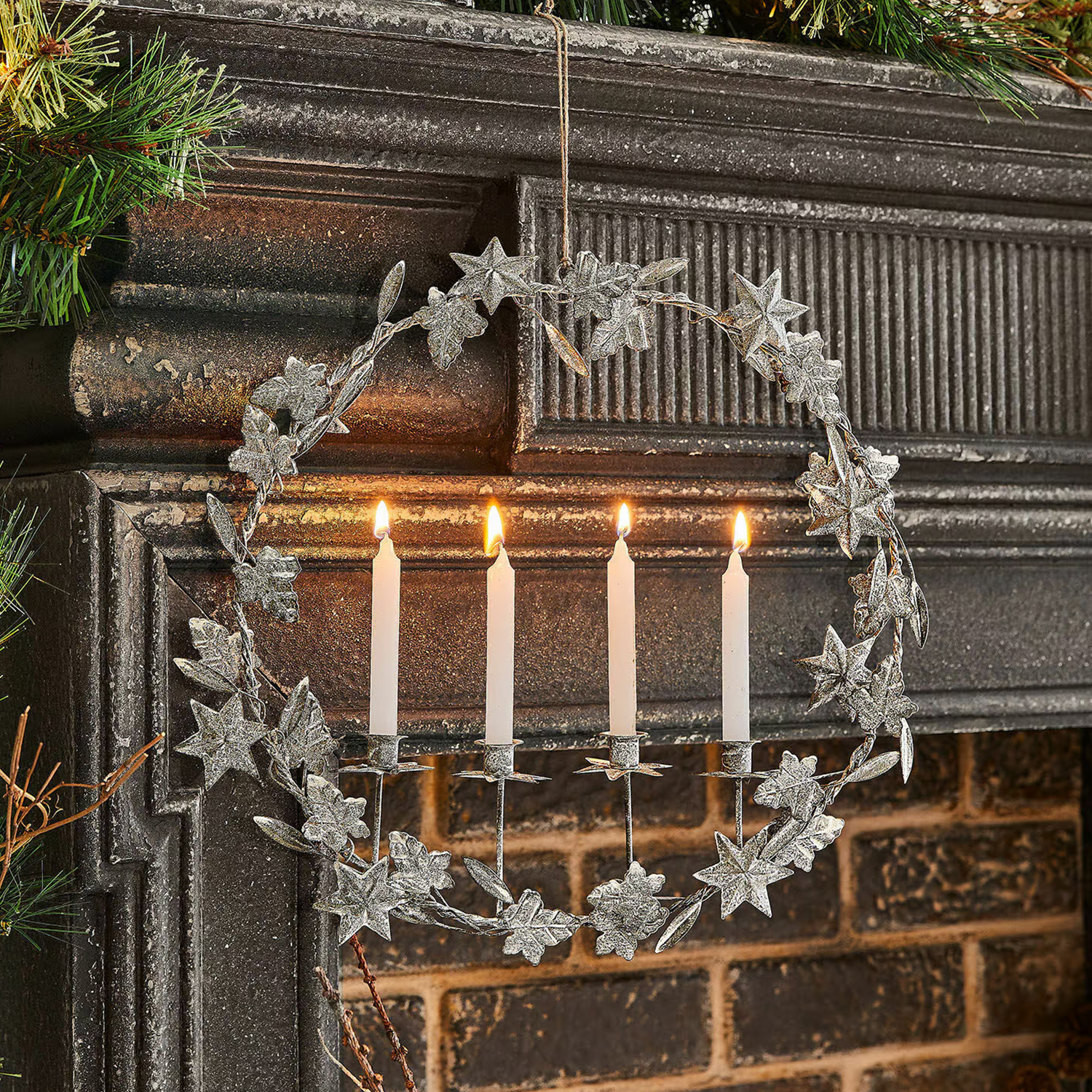 Metallkranz mit Blättern und vier weißen brennenden Kerzen an einem Kamin, Weihnachtsdekoration