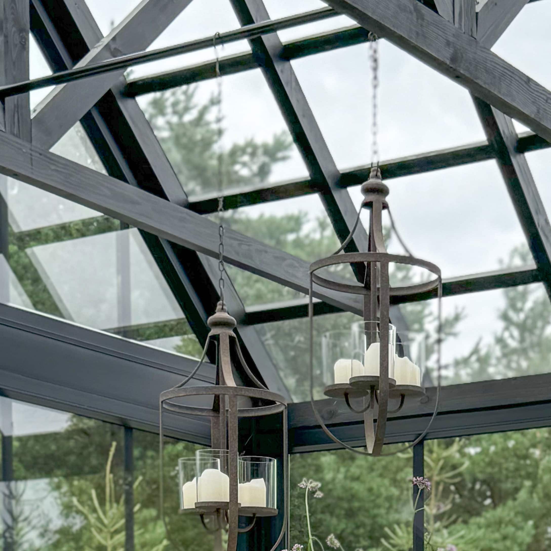 Hängende Laternen aus rostfarbenem Metall mit weissen Kerzen in einer hellen Orangerie