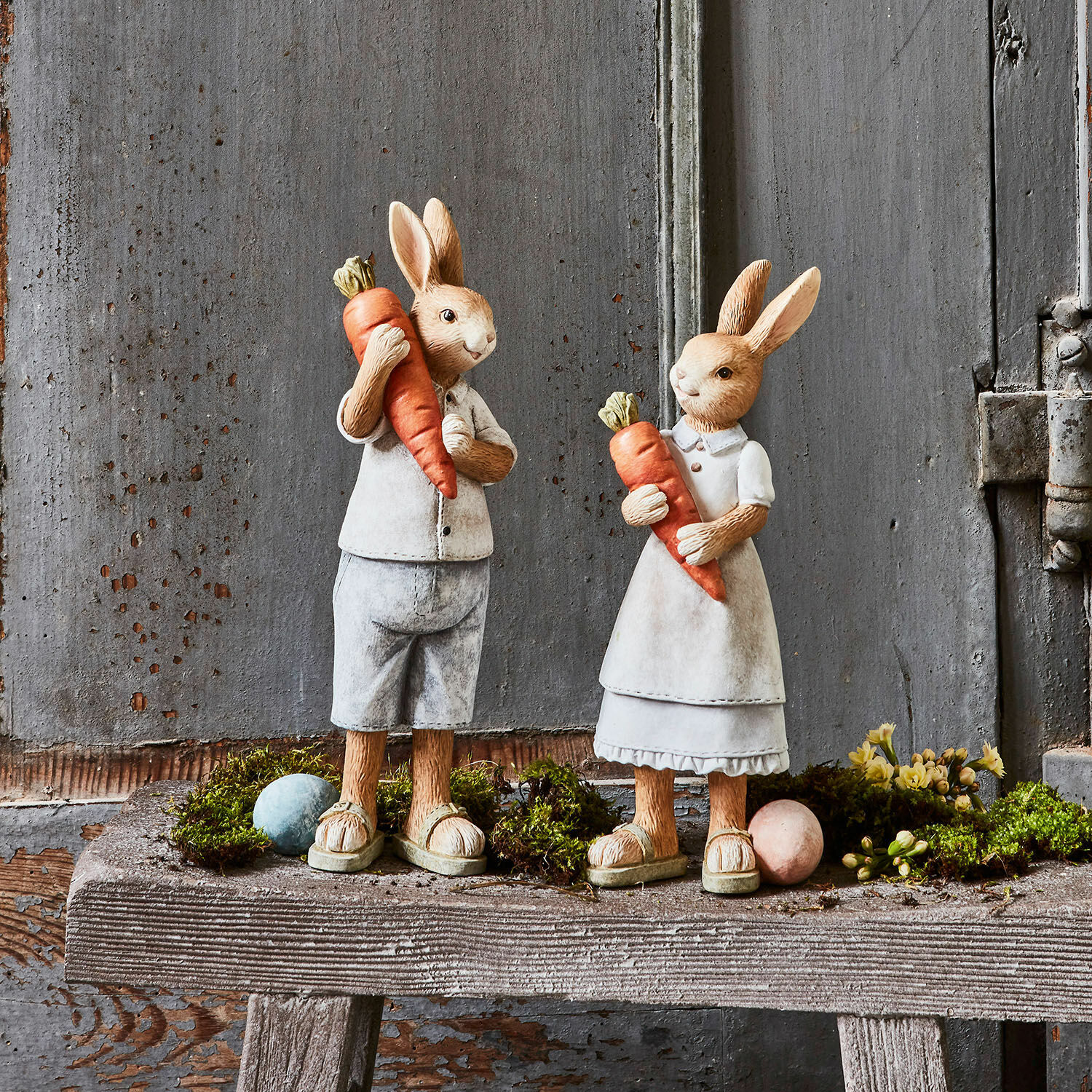 Hase 2er Set Gimont Figuren aus Hasenmaterial in beiger Kleidung mit orangen Karotten auf rustikaler Holzbank