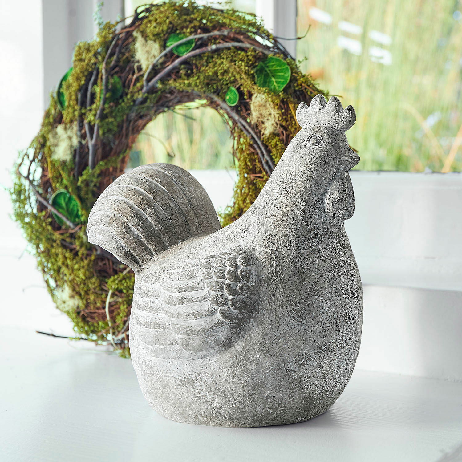 Deko-Henne Roselique Graue Hühnerfigur aus Beton als Dekoration vor hellem Hintergrund mit grünem Kranz