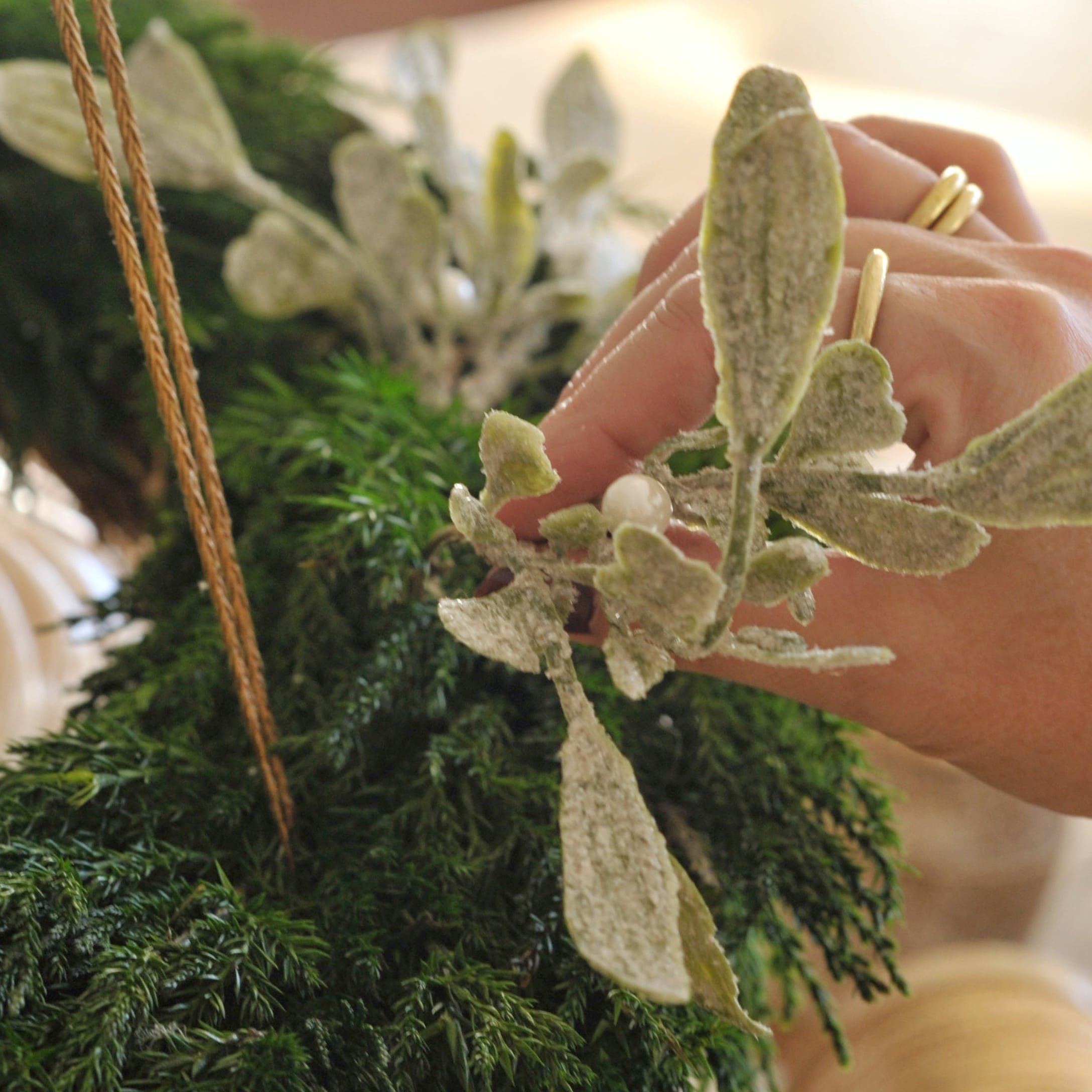 Handdekorierter weisser Adventskranz mit grünen und weissen Blättern sowie Perlenornamenten