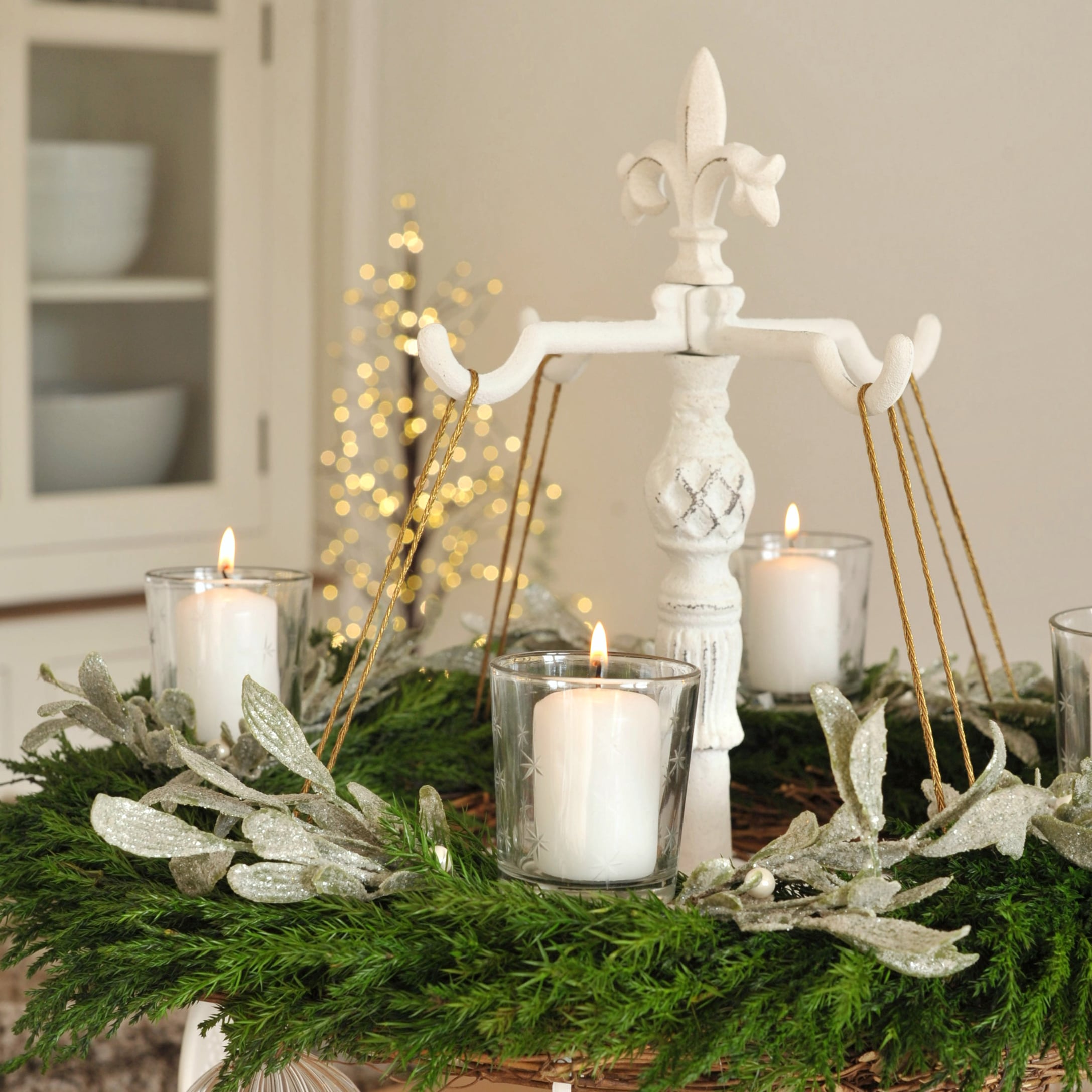 Weisser Metallständer mit grünem Adventskranz und brennenden Kerzen in Glasbehältern