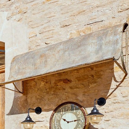Metallene, rostfarbene Vintage-Markise über einer Uhr an einer Steinwand mit Wandlampen