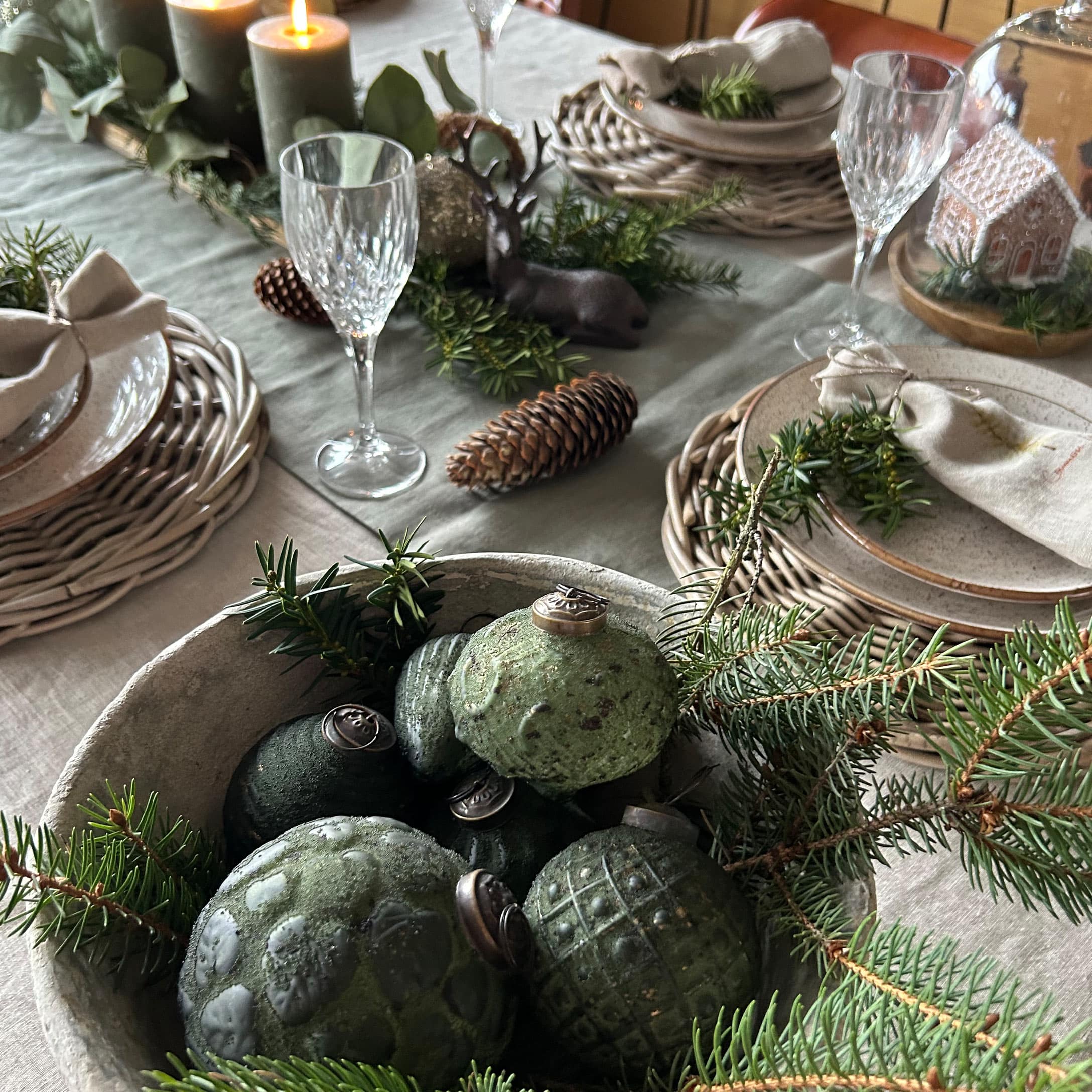 Grüne Keramik-Weihnachtskugeln in einer Schale mit Tannenzweigen auf einem festlich gedeckten Tisch