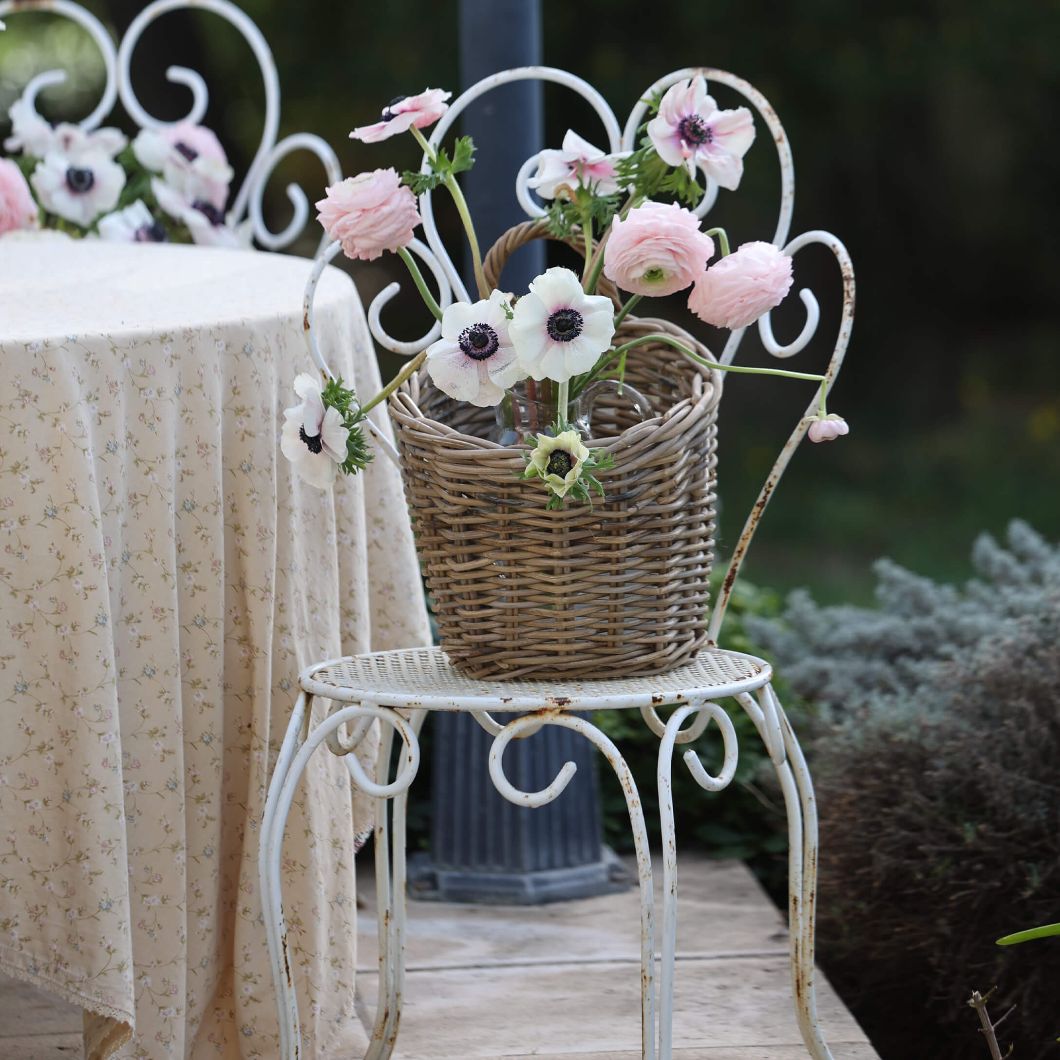 Weidenkorb mit rosa und weissen Blumen auf weissem Metallstuhl im Garten