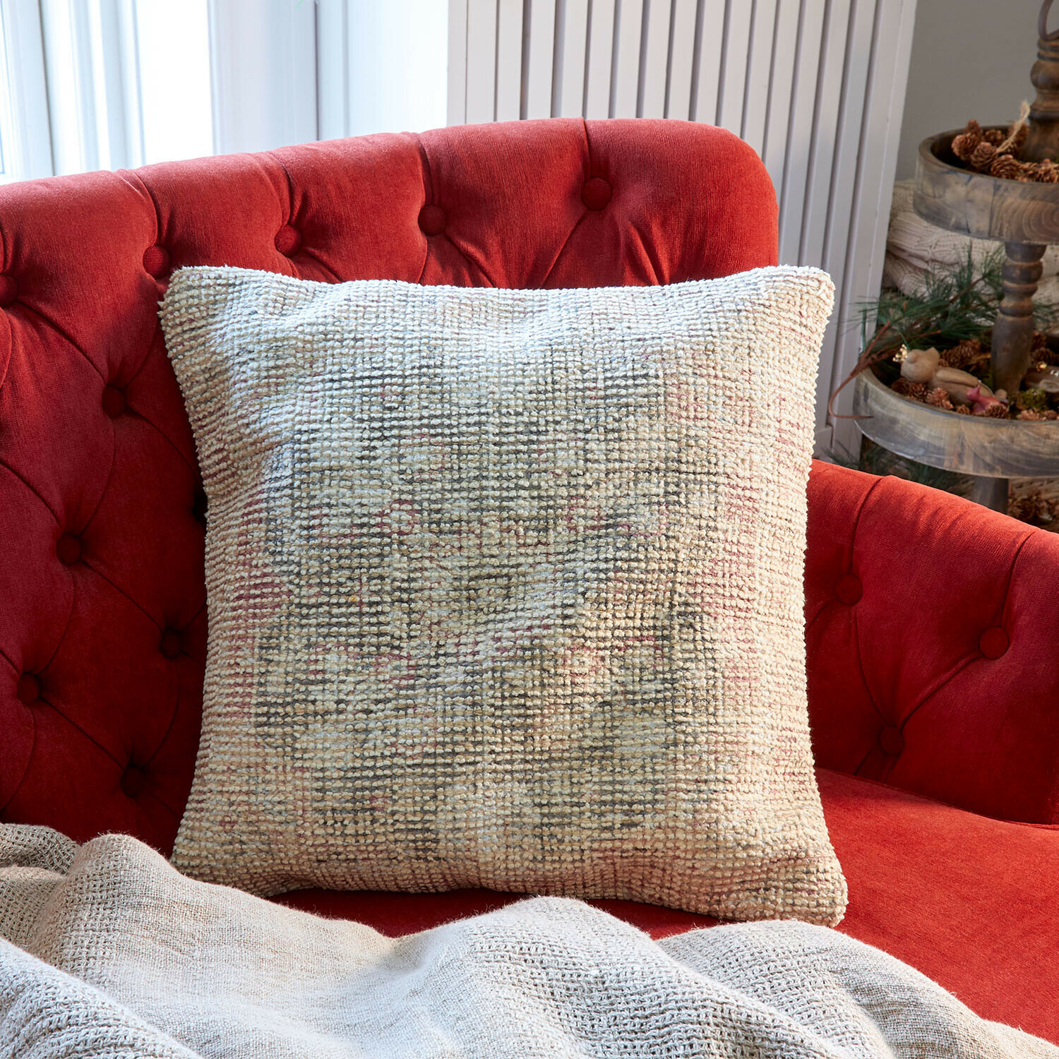 Beiges dekoratives Kissen aus weichem Stoff auf rotem, gepolstertem Sofa im Wohnzimmer