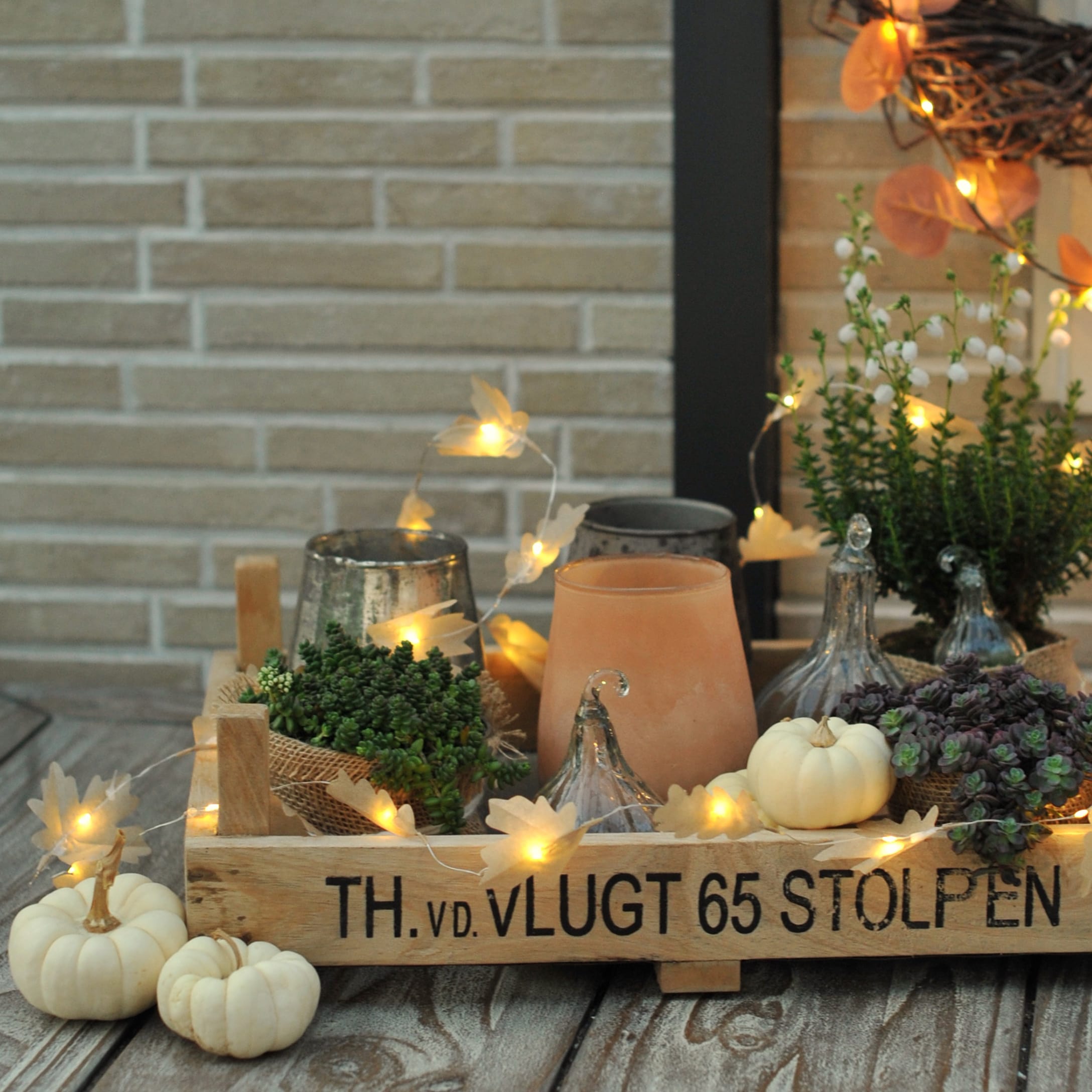 Holztablett mit herbstlicher Dekoration, weissen Kürbissen, Pflanzen und LED-Lichterkette auf Holztisch