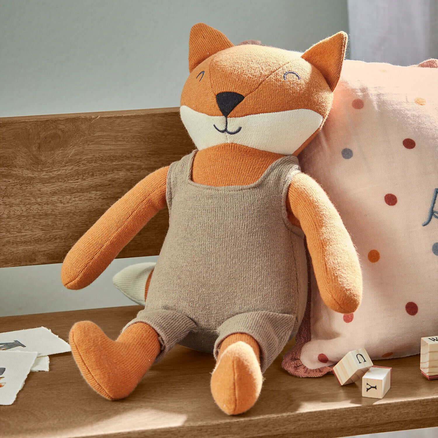 Weiches Stofftier Fuchs in beiger Latzhose auf Holzbank mit Lernspielzeug aus Holz