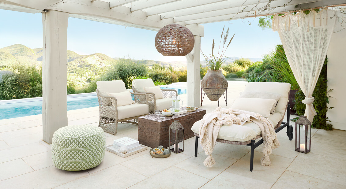 Weisses Gartenmöbel-Set mit Polstern unter Pergola am Pool, natürliche Dekorationen und Laternen