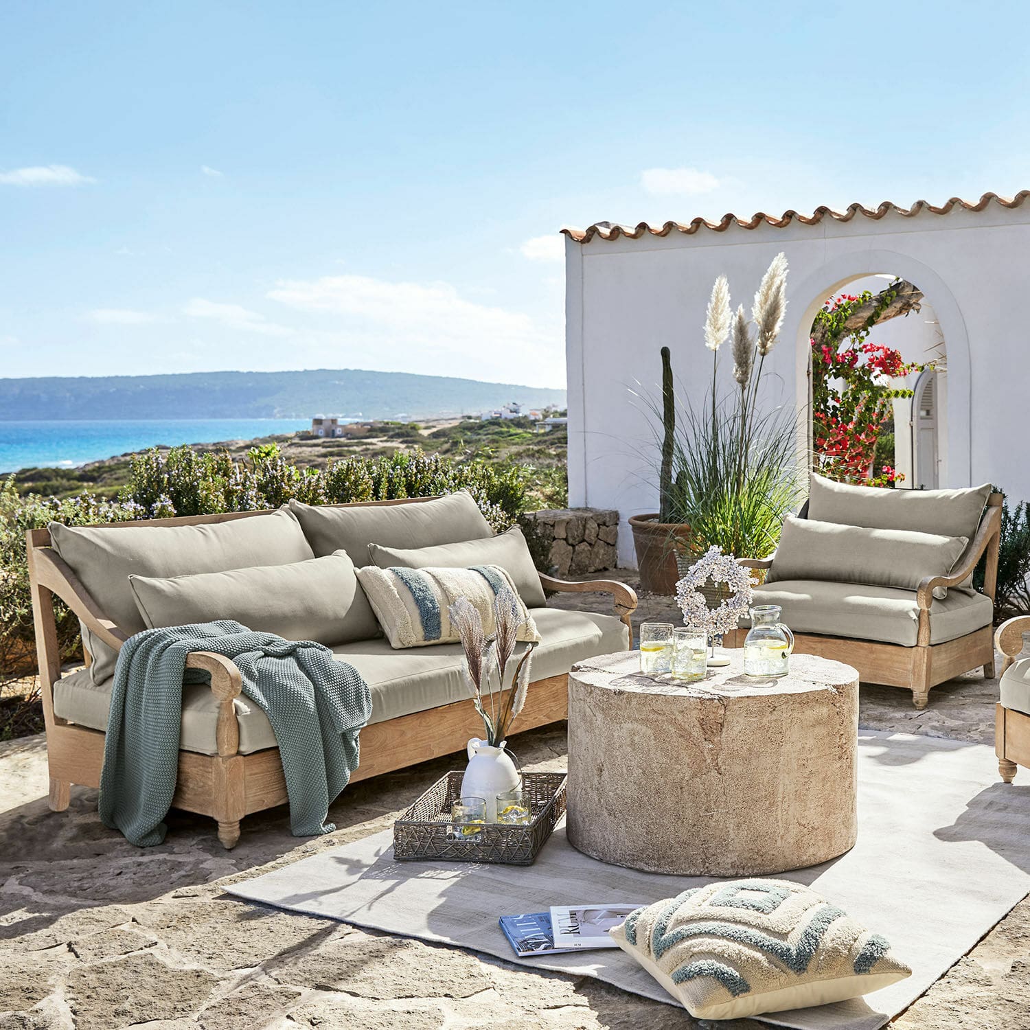 Sitzgruppe Montcassin Gartenmöbel-Set aus hellem Holz mit beigen Polstern auf steinerner Terrasse mit Meerblick
