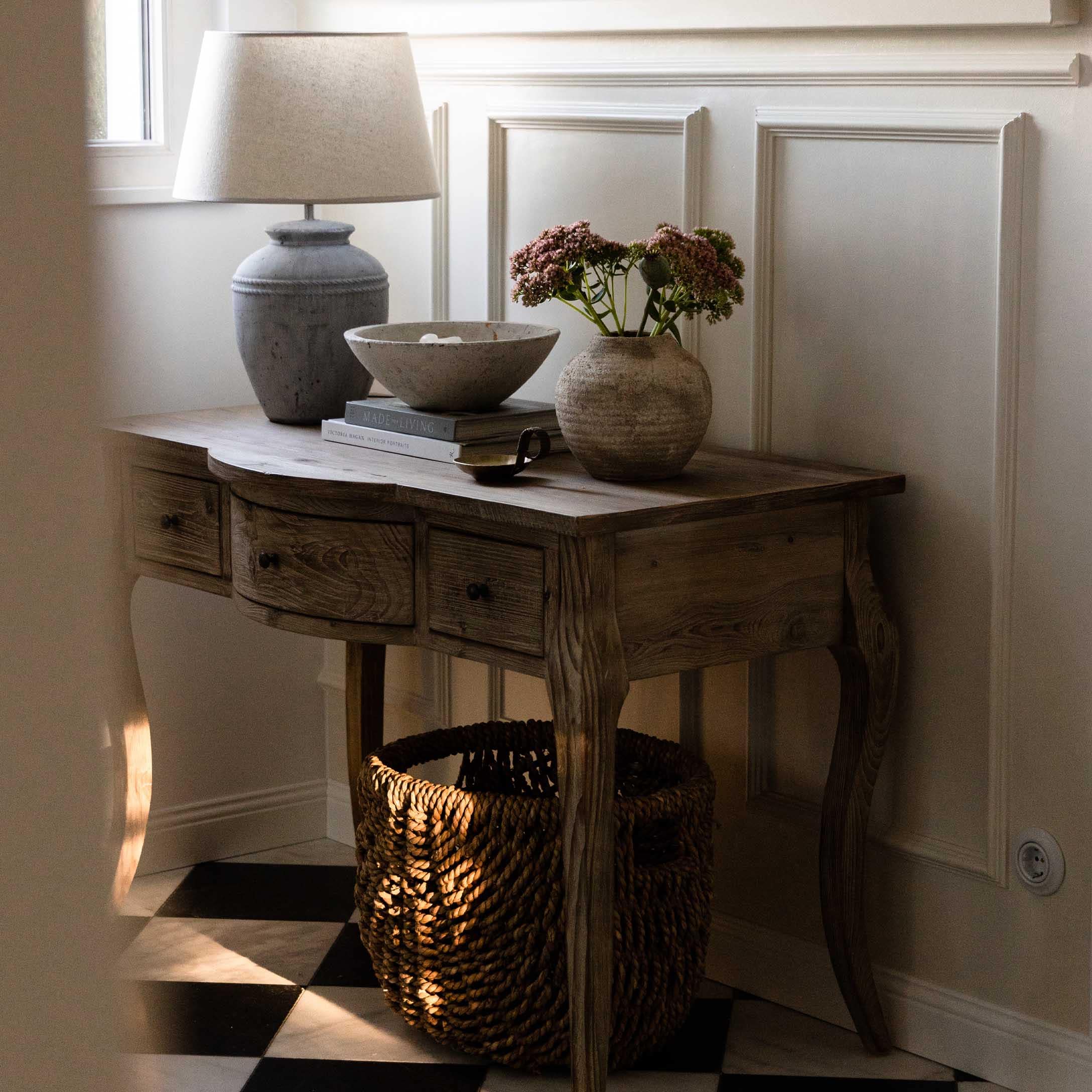 Holztisch mit Schubladen, Lampe, Vase und Korb auf schwarz-weiss kariertem Boden