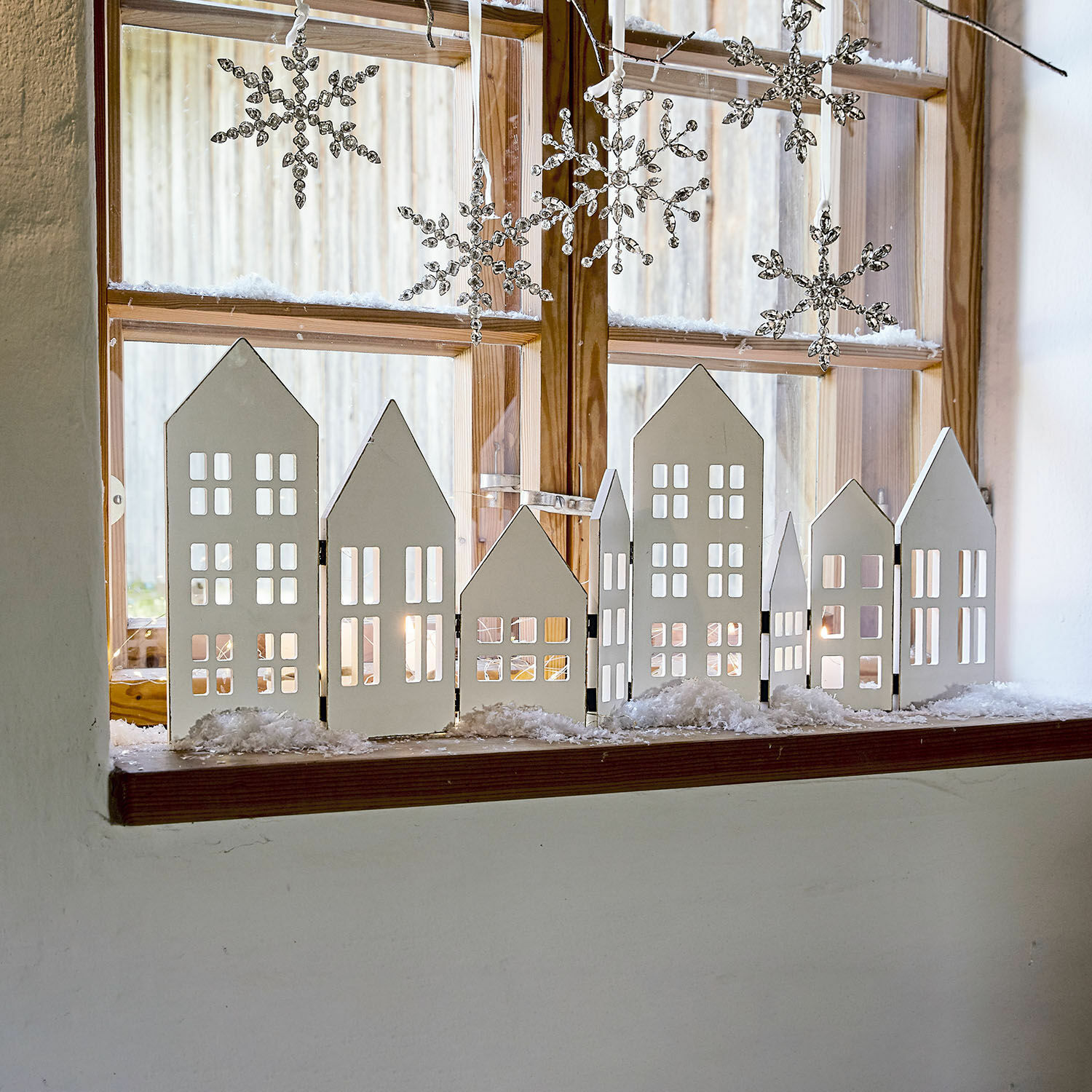 Deko-Shutter Cottages Weisse Holzhausdekoration auf der Fensterbank mit hängenden Schneeflocken für winterliche Stimmung