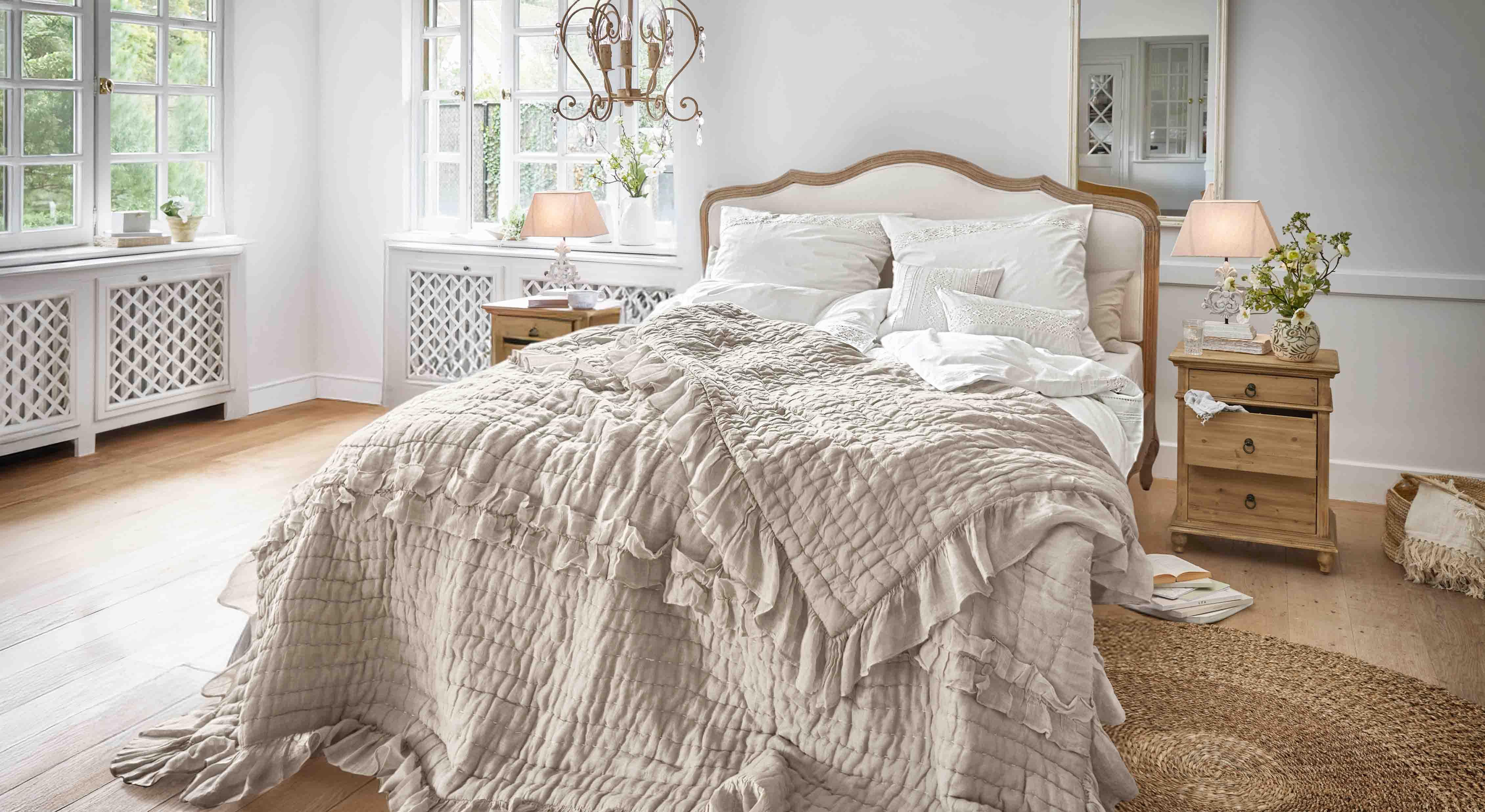Gemütliches Schlafzimmer mit Bett in beiger Rüschendecke und hellen Holznachtischen