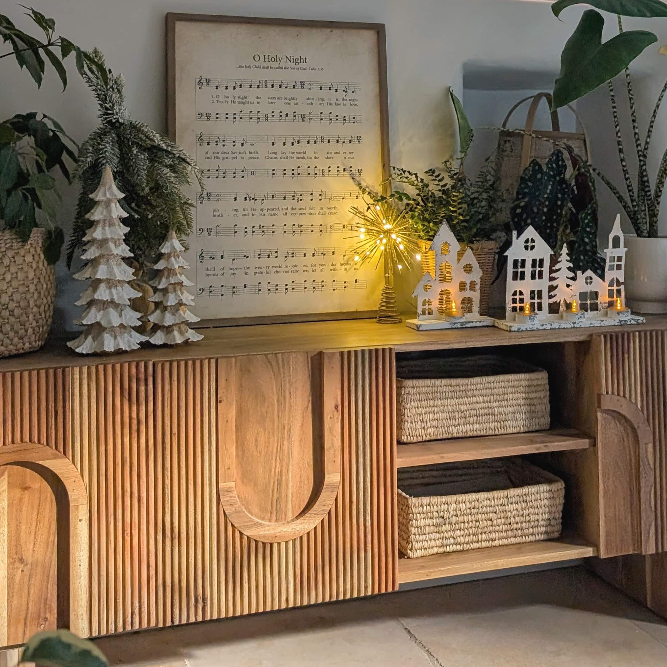 Holzkommode mit Weihnachtsdekoration, weissen Häusern und beleuchteten LED-Tannenbäumen