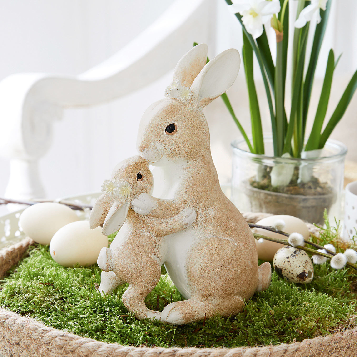 Hasen Aliena Figuren von zwei beige-weissen Hasen mit Blumenkränzen auf grünem Moos, österliche Dekoration