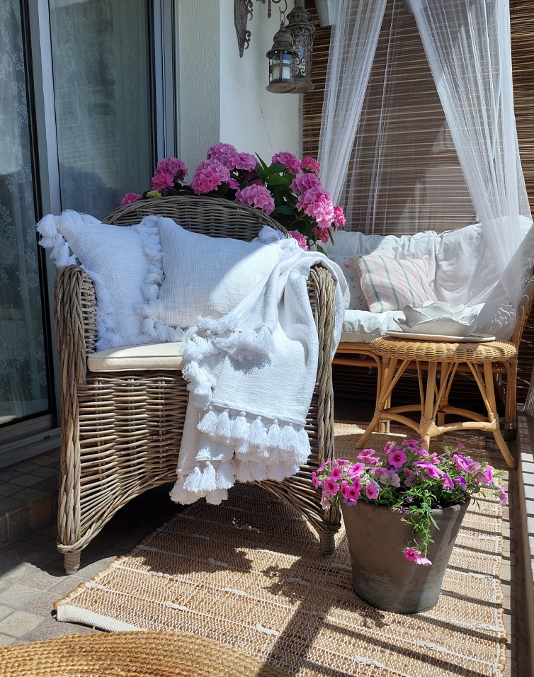 Gemütlicher Balkon mit Rattansessel, weisser Decke und pinken Blumen, natürliche Dekoration