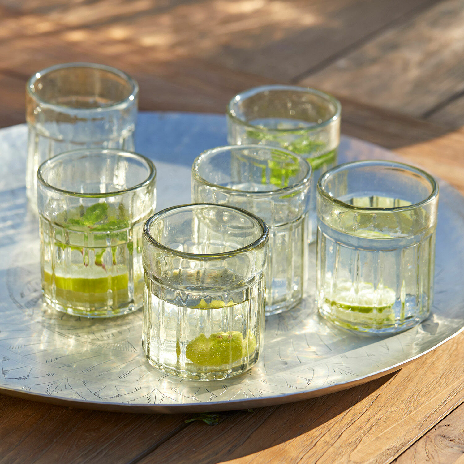 Glas 6er Set Roseville Sechs durchsichtige Gläser mit Limettenstücken auf einer Metallplatte auf einem Holztisch