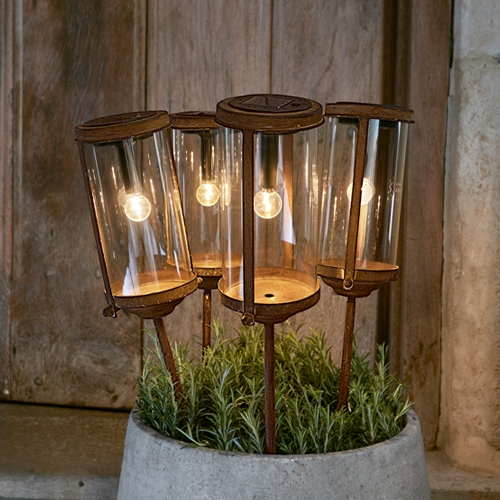 Set mit vier Gartenlampen aus Glas und rostigem Metall in einem Topf mit grünen Pflanzen, dekorative Aussenbeleuchtung