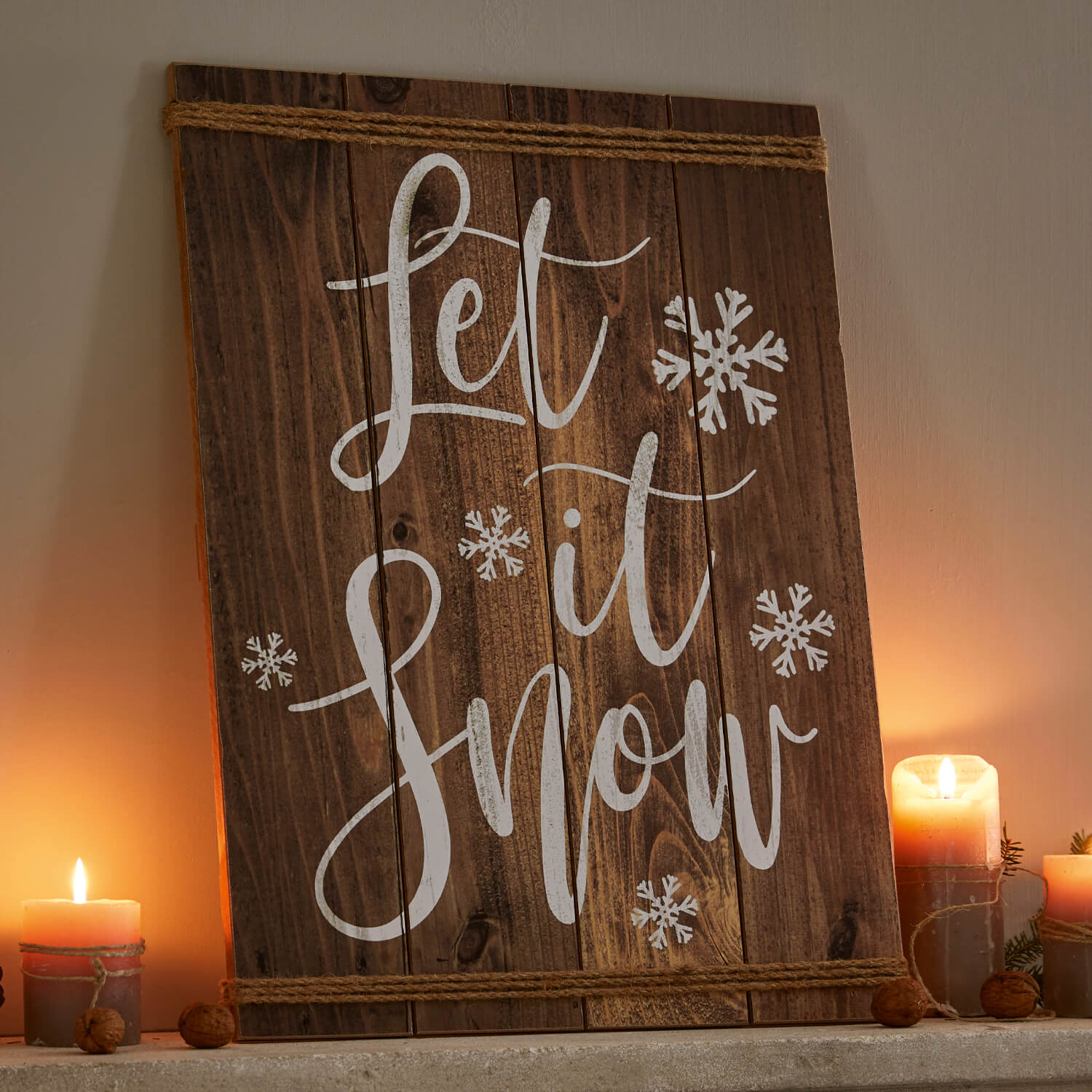 Holz-Wanddekoration mit Schriftzug Let it Snow und weißen Schneeflocken, umgeben von Kerzenlicht