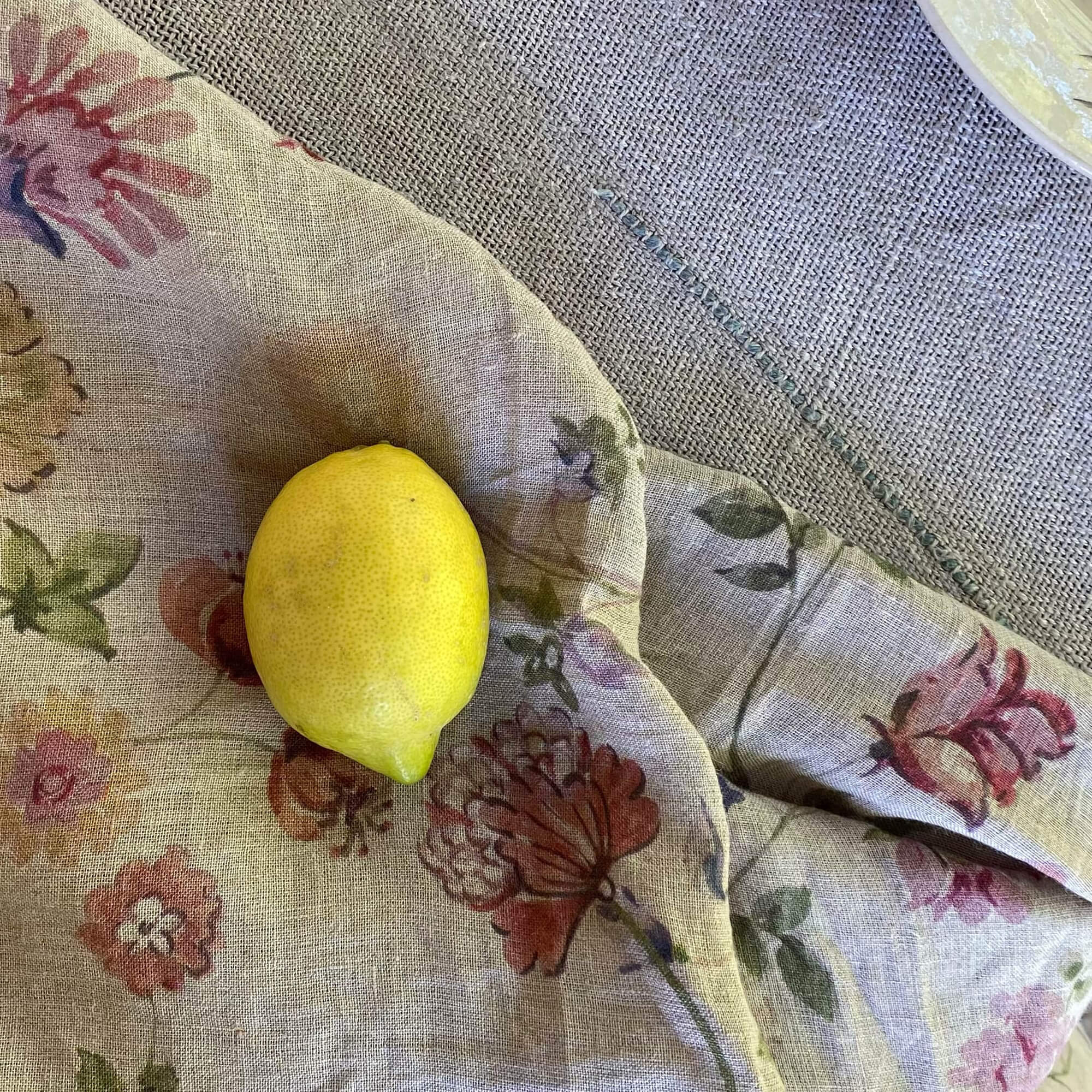 Leinentischdecke mit pastellfarbenem Blumenmuster und gelber Zitrone darauf auf dem Tisch