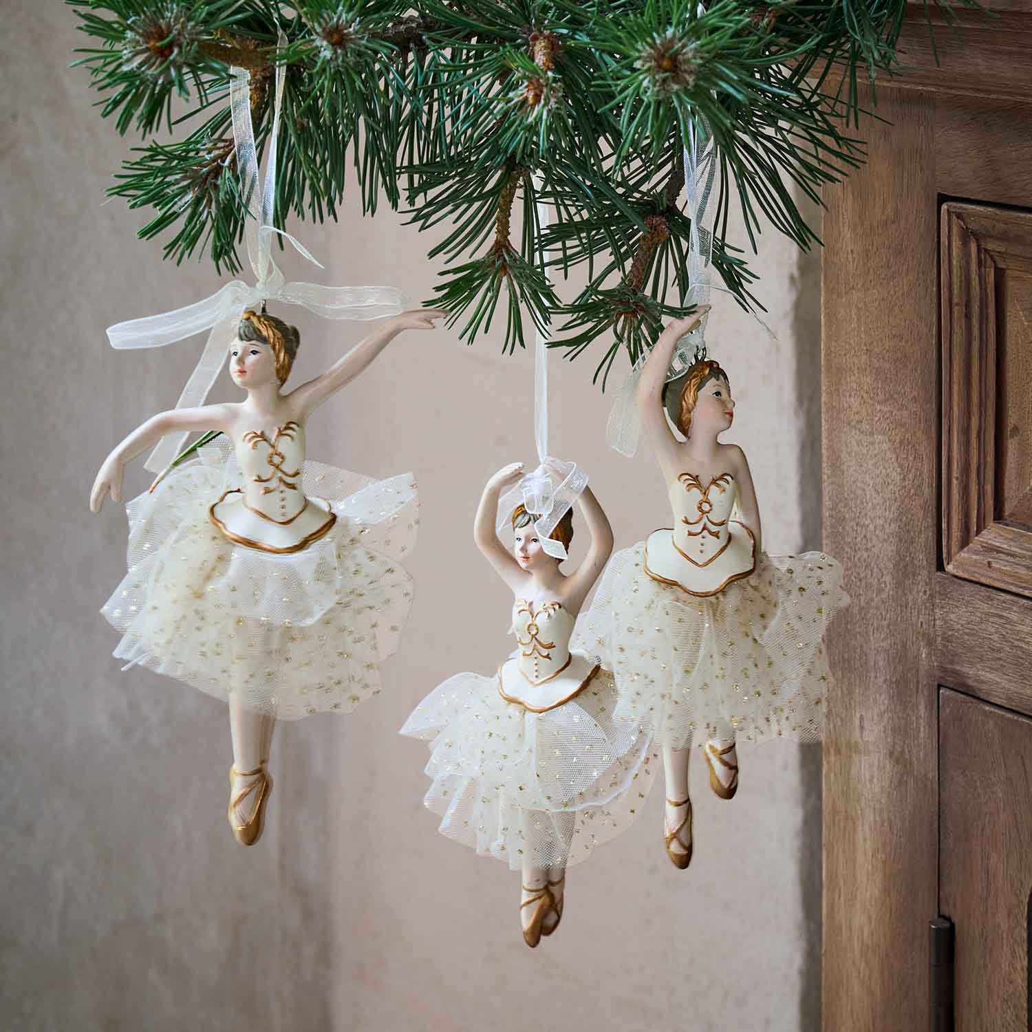 Drei weisse Ballerina-Figuren mit Tüllröcken und goldenen Details an einem Tannenzweig hängend