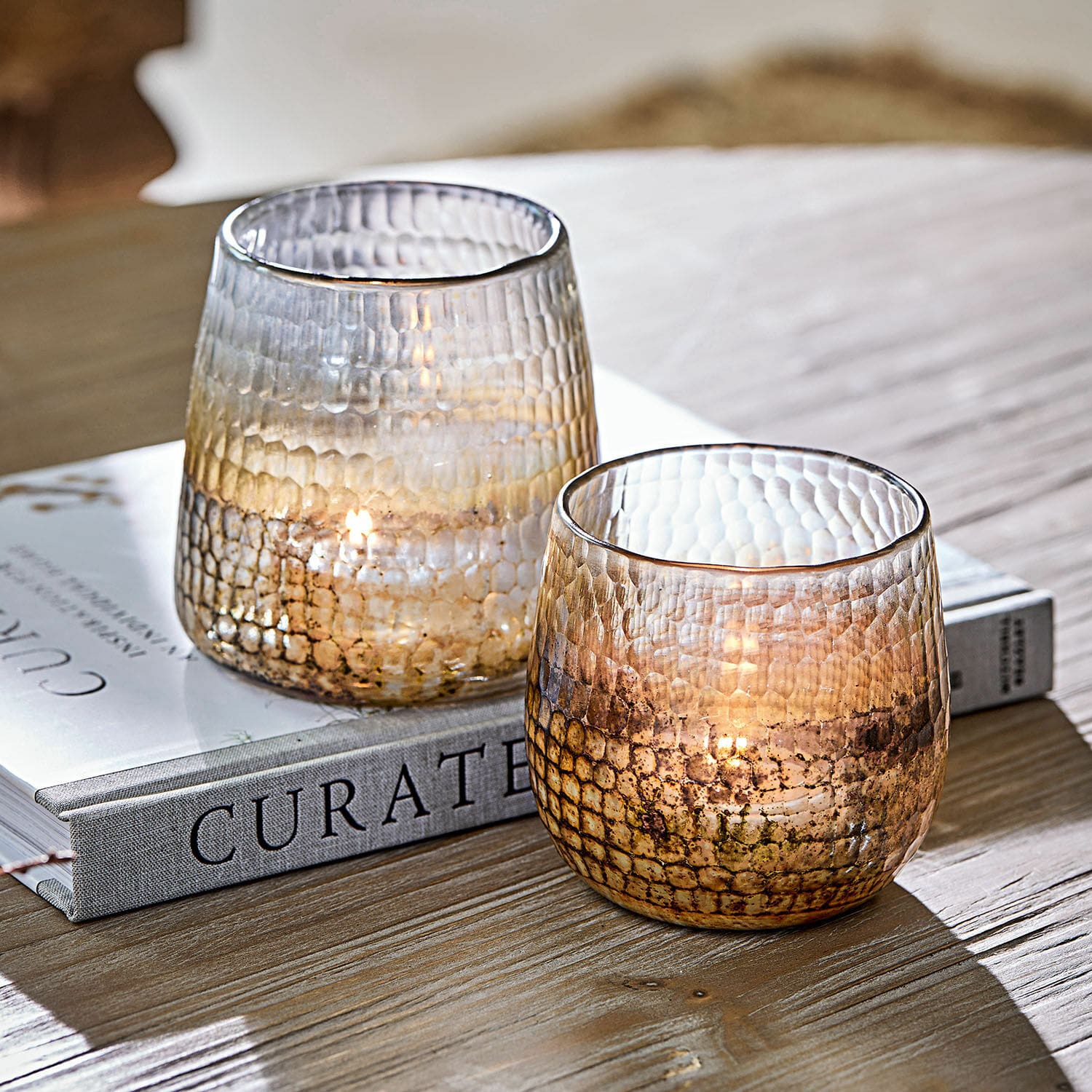 Windlicht 2er Set Agnús Zwei strukturierte Glas-Teelichthalter in Braun auf einem Holztisch neben einem Buch