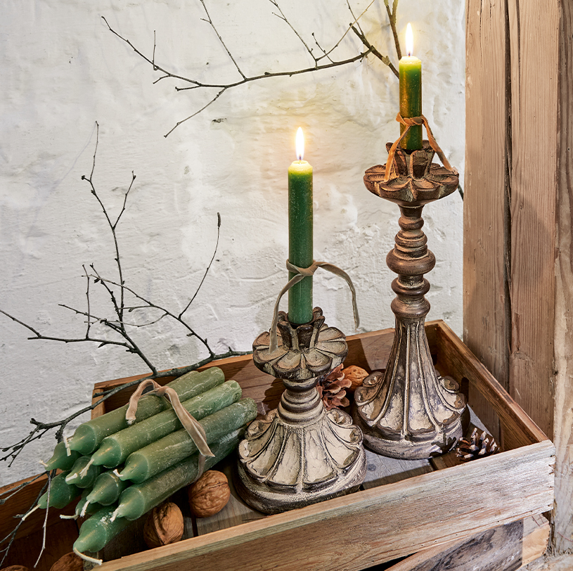 Zwei dekorative Kerzenhalter mit grünen Kerzen auf Holztablett mit Nüssen und Zweigen