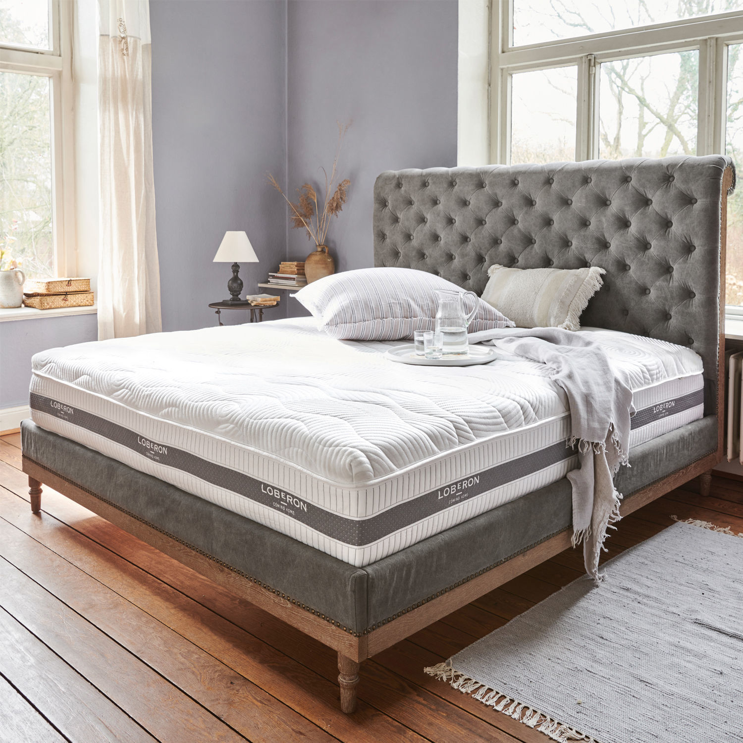 Matratze mit Topper 180x200 Raillimont Bett mit grauem Polsterkopfteil und weisser Loberon-Matratze in hellem Raum mit Holzboden