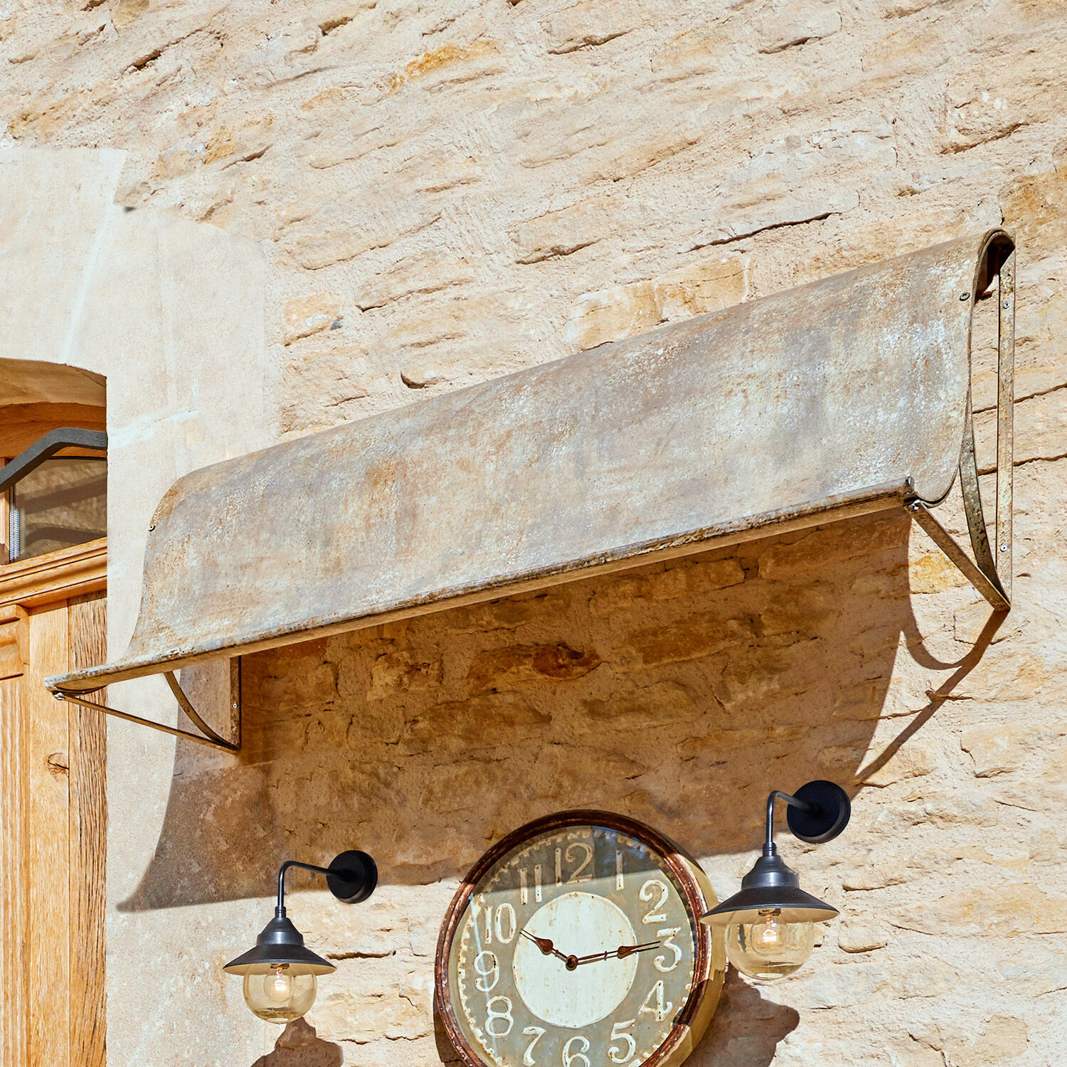 Vordach Lison Verwittertes graues Metallvordach an einer Steinmauer mit antiker Uhr und schwarzen Lampen