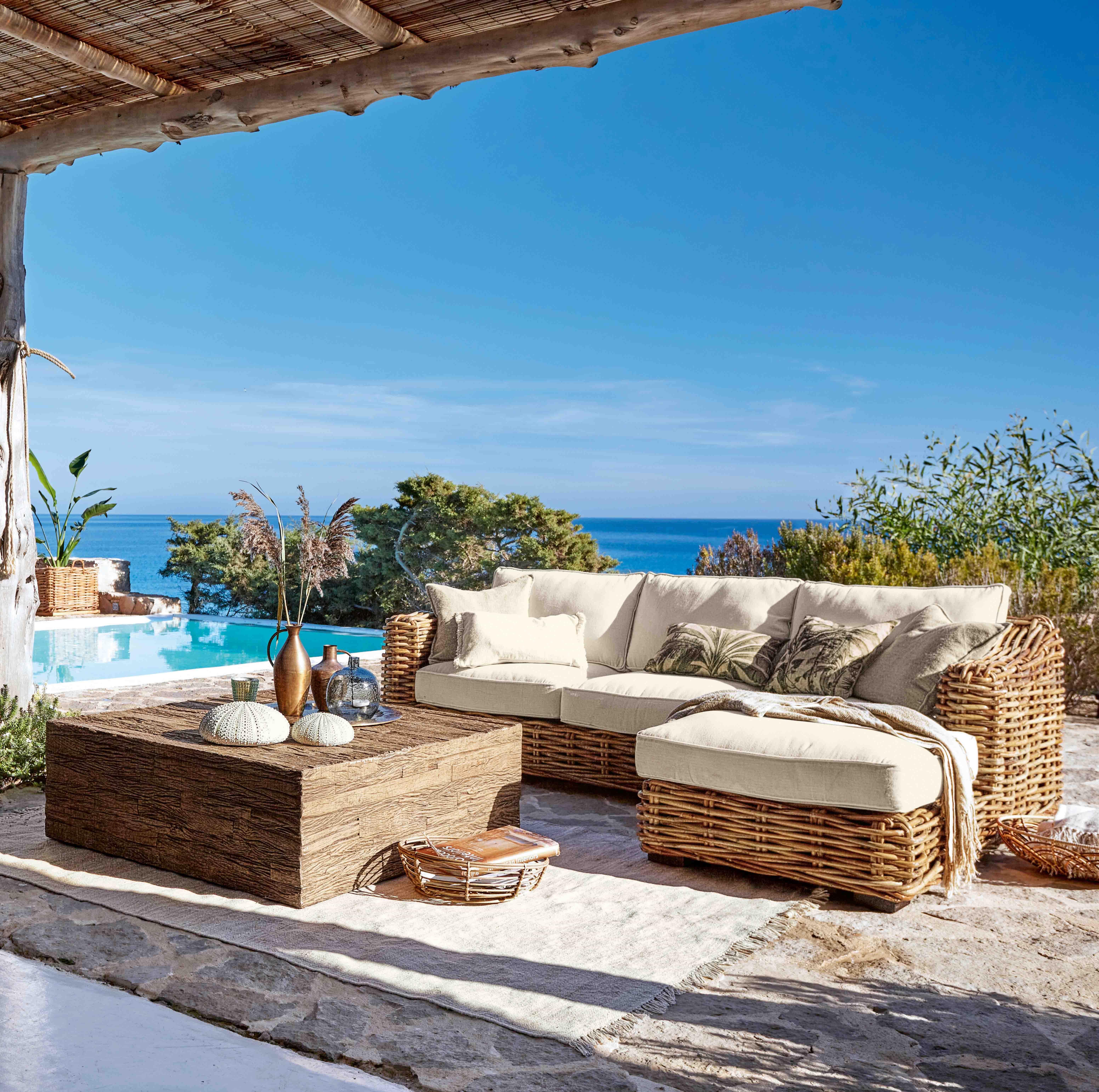 Rattan-Gartenmöbel mit cremefarbenen Polstern, Blick auf Pool und Meer, Outdoor-Lounge