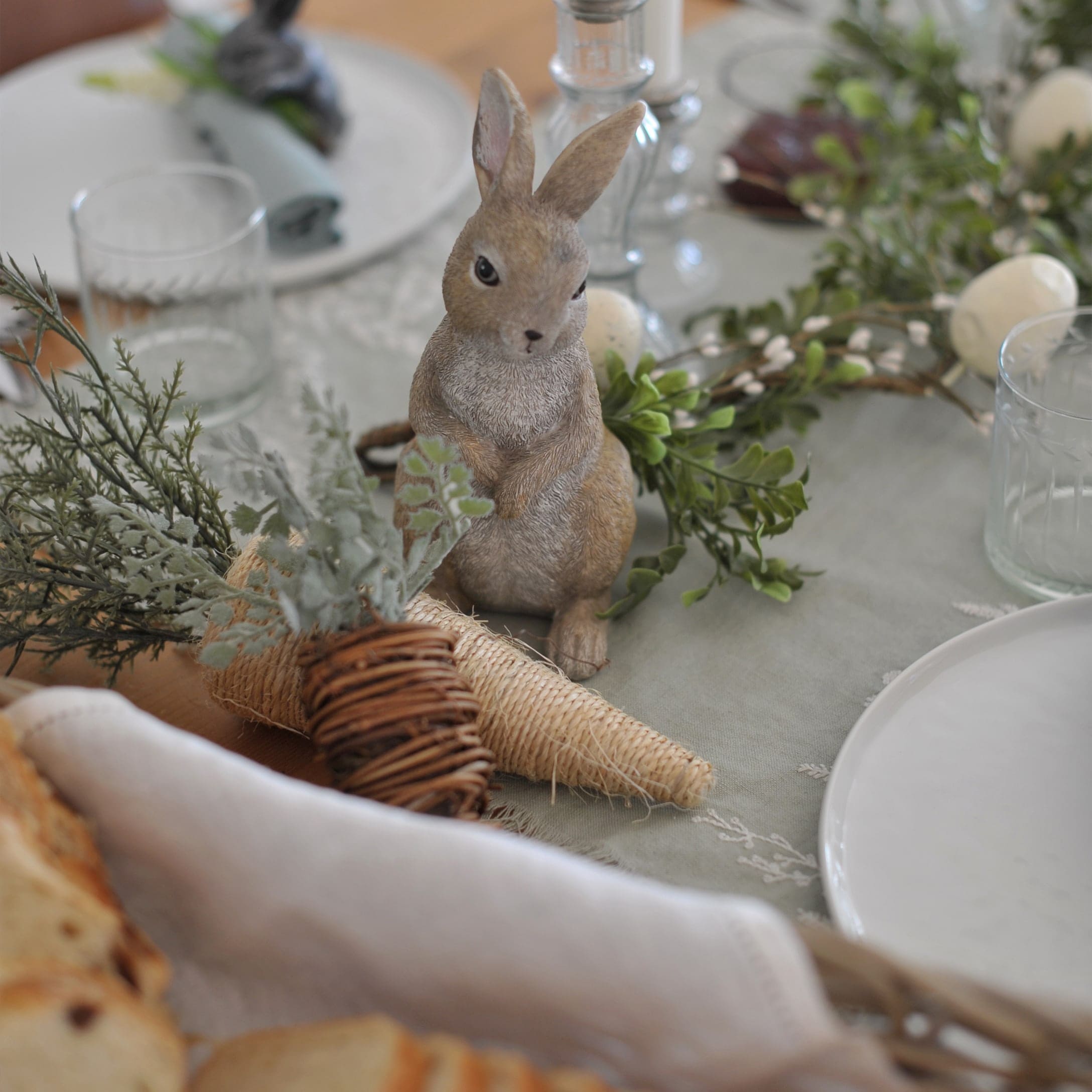 Dekorativer Hase auf dem Tisch mit natürlichen Deko-Elementen und Glas, Frühlingsdekoration