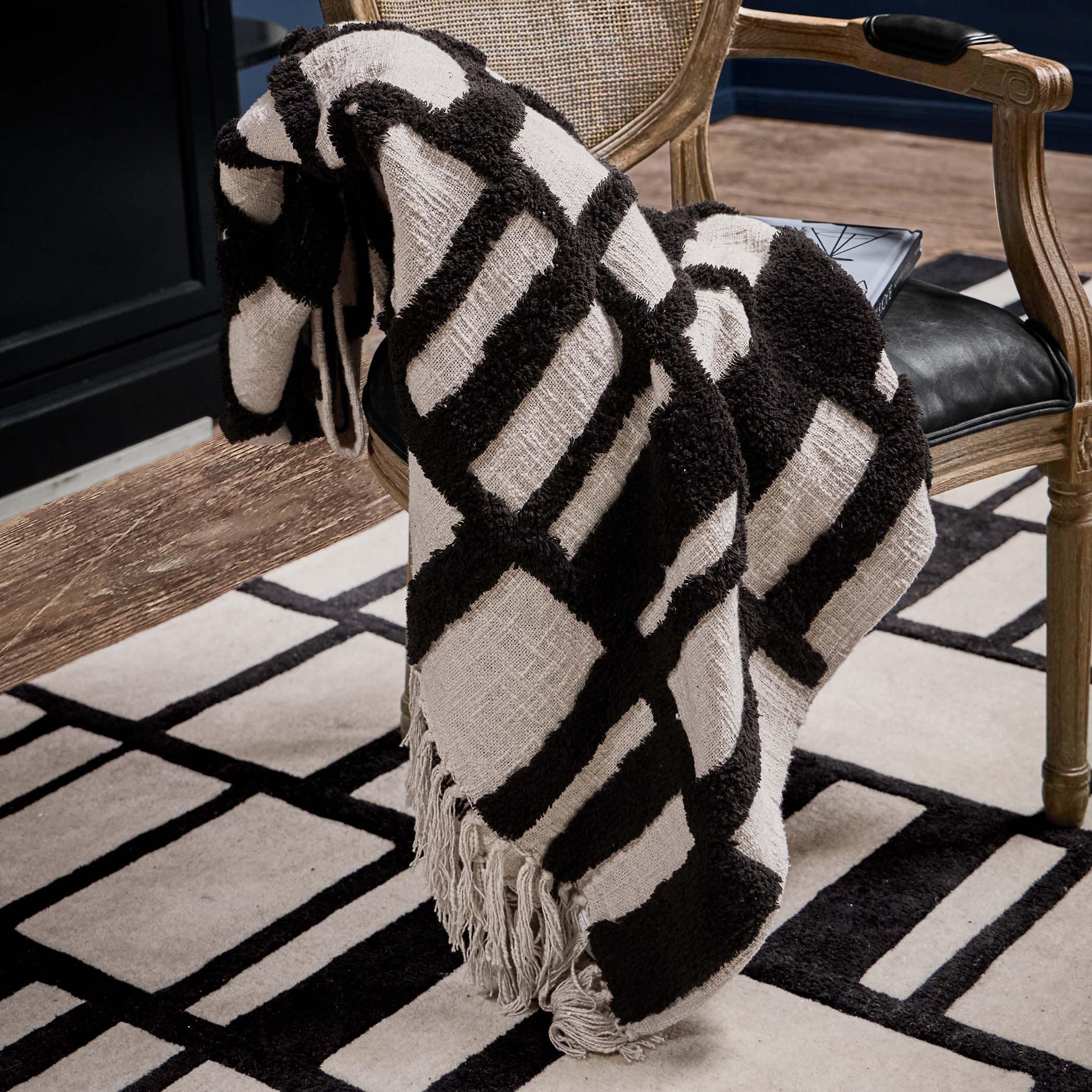 Schwarz-weisses Plaid mit geometrischem Muster aus weichem Stoff auf Holzstuhl im Wohnzimmer