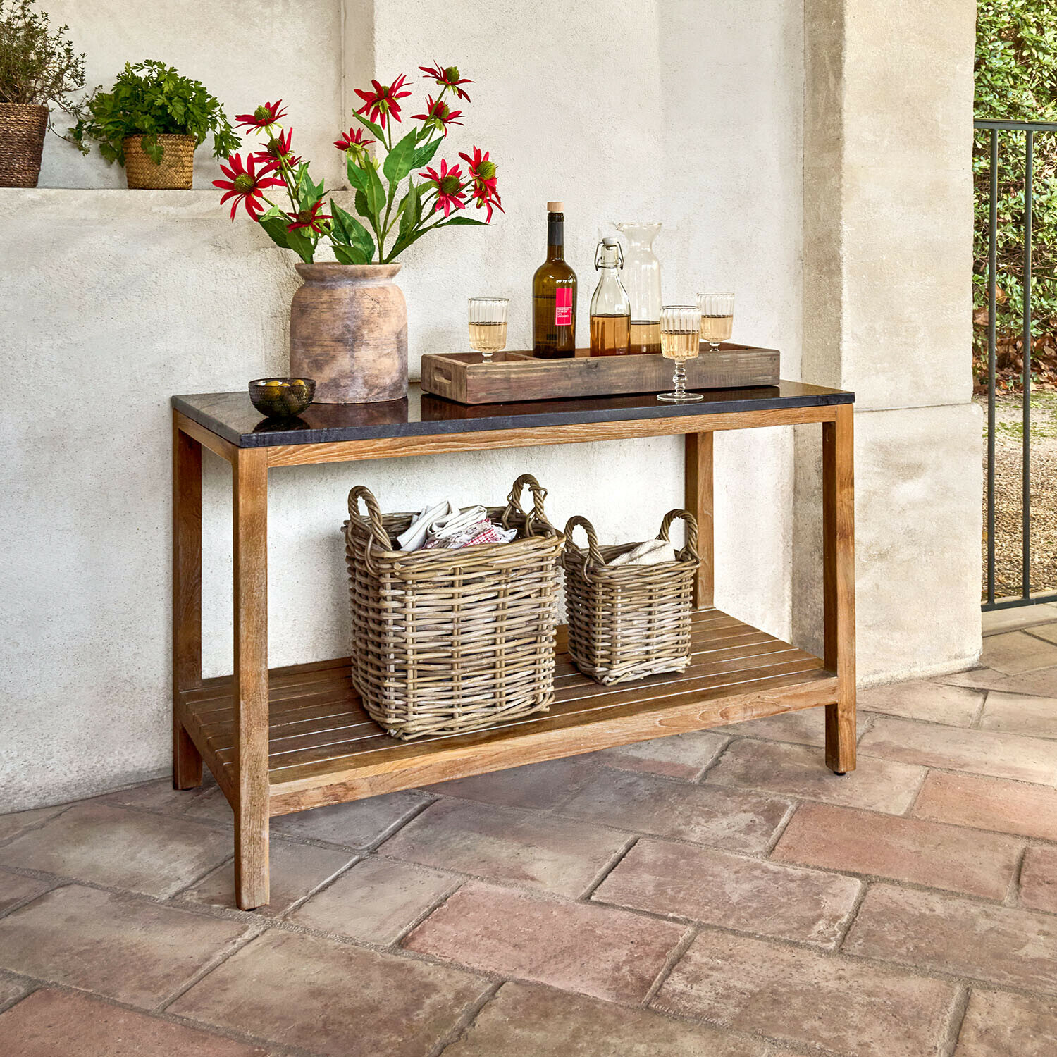 Konsole mit Holzrahmen und schwarzer Tischplatte, dekoriert mit Vase und roten Blumen sowie Weidenkörben darunter