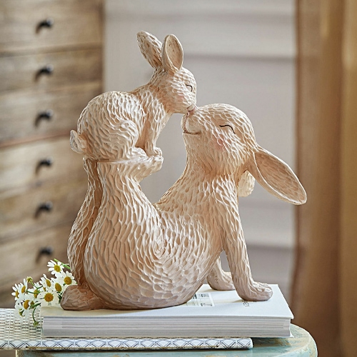 Beige Keramikfigur zweier sich aneinander kuschelnder Hasen auf Büchern, zarte Frühlingsdekoration für zu Hause