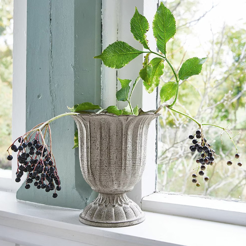 Graue Keramikvase mit grünen Blättern und schwarzen Beeren auf der Fensterbank dekoriert