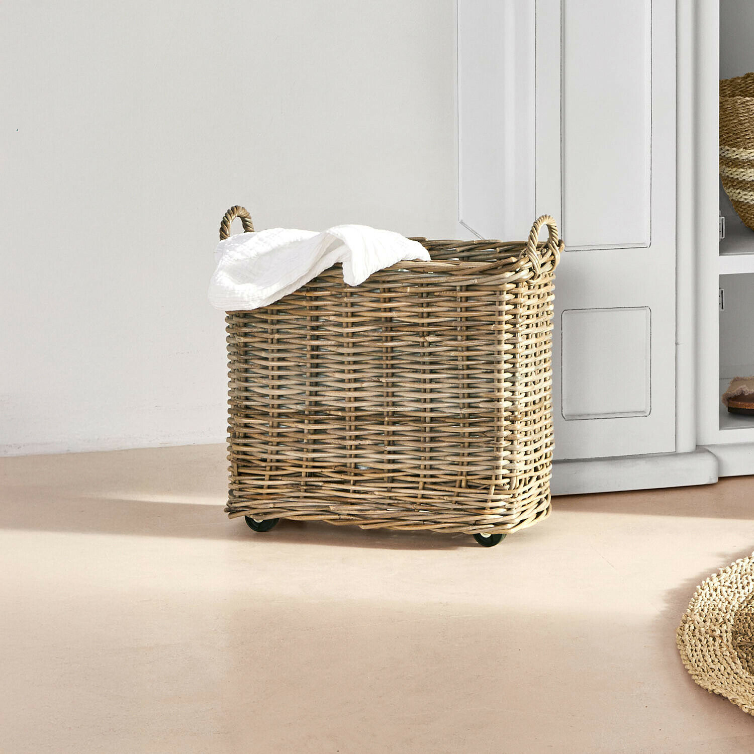 Wäschekorb aus natürlichem Weidengeflecht auf Rollen mit weissem Handtuch in hellem Raum