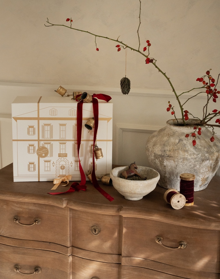 Weihnachtliche Dekoration mit weisser Geschenkbox, roten Bändern und natürlicher Keramik auf Holzkommode