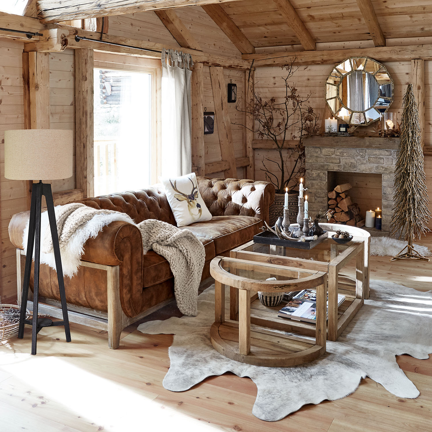 Gemütliches Wohnzimmer mit braunem Ledersofa, Holztischen und rustikalem Steinkamin