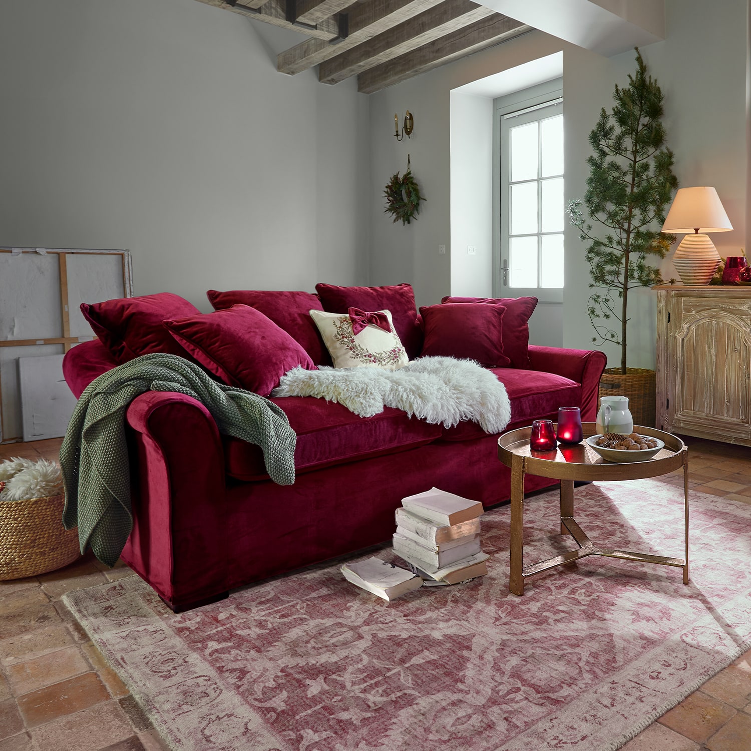 Rotes Samtsofa mit Kissen und weicher Decke in gemütlichem Wohnzimmer mit Holztreppe