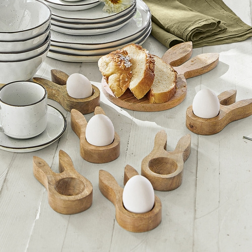 Holz-Eierhalter in Hasenohrenform auf weissem Tisch mit Brot und Geschirr